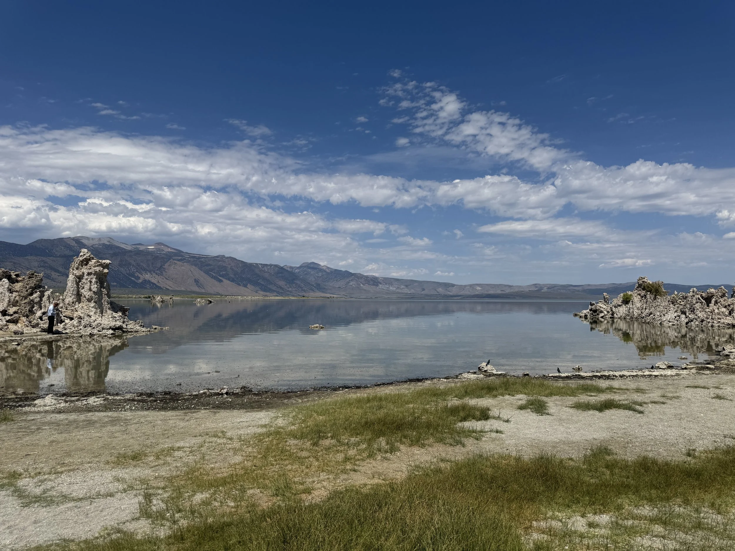Wide view across Mono Lake framed by tufa formations, mountain ridges, and cloud reflections.