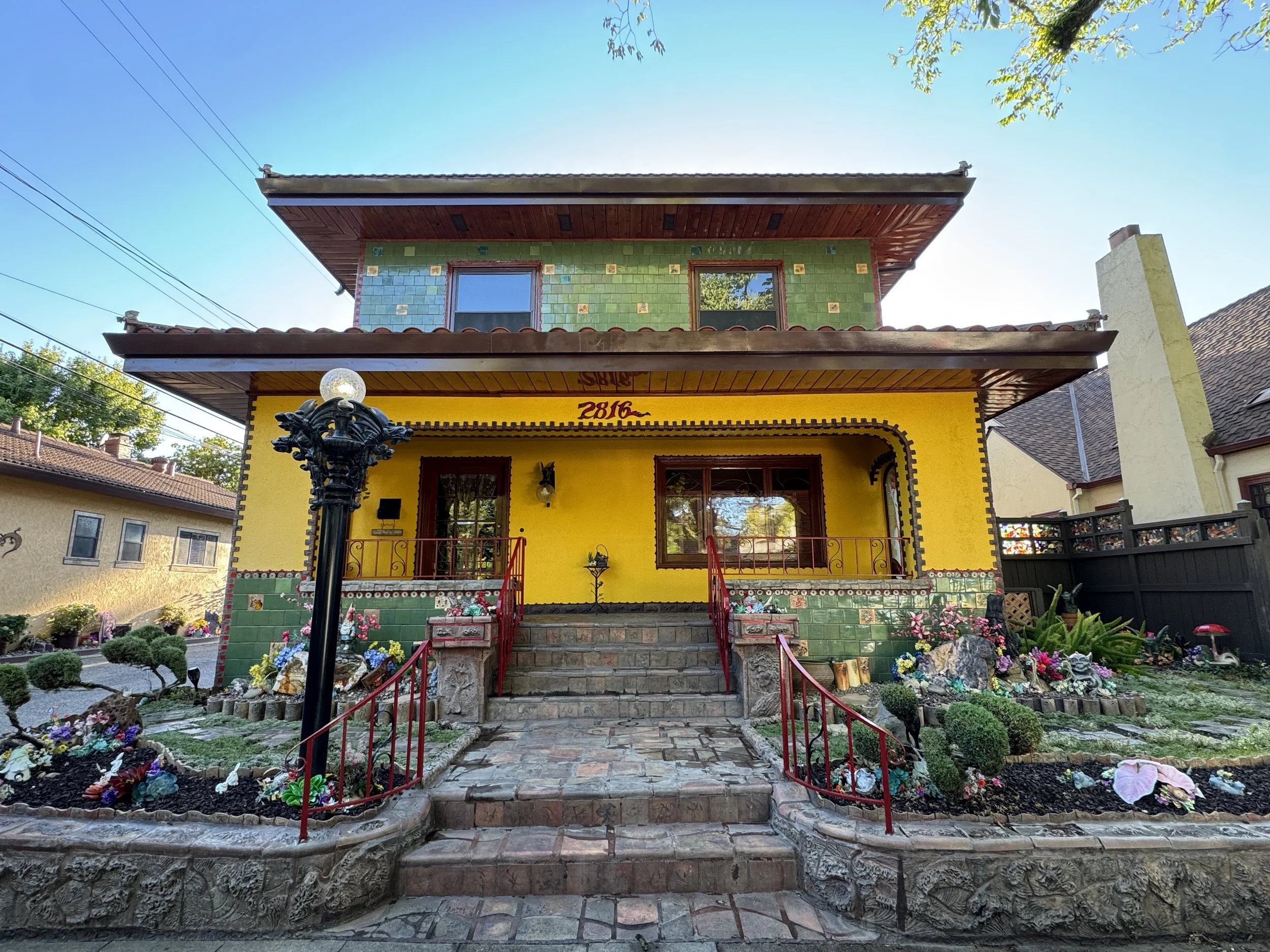 Bright yellow and green exterior of Sacramento’s Dragon House surrounded by mosaics and elaborate garden art.