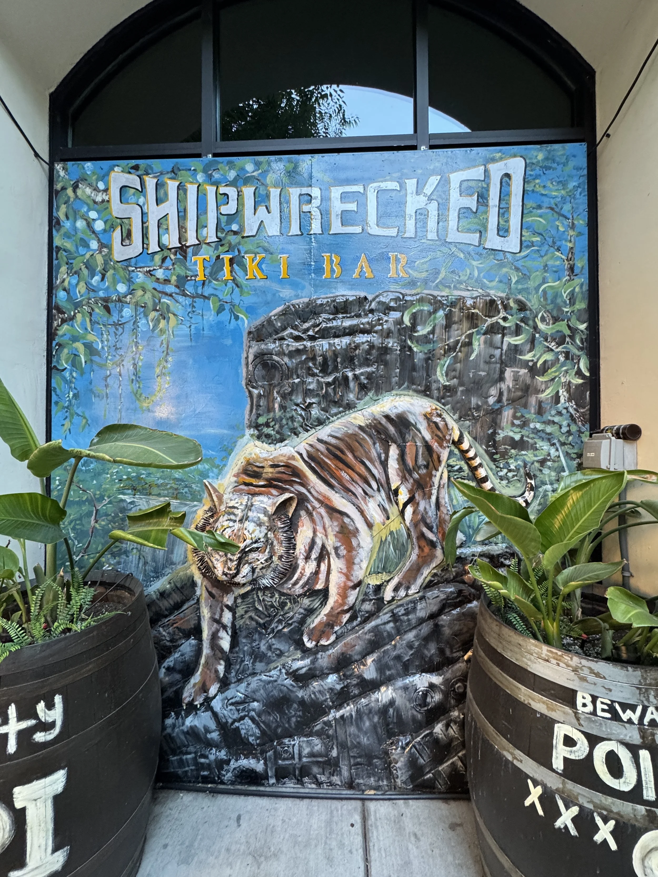 Hand-painted Shipwrecked Tiki Bar entrance display featuring a tiger, tropical plants, and barrels.