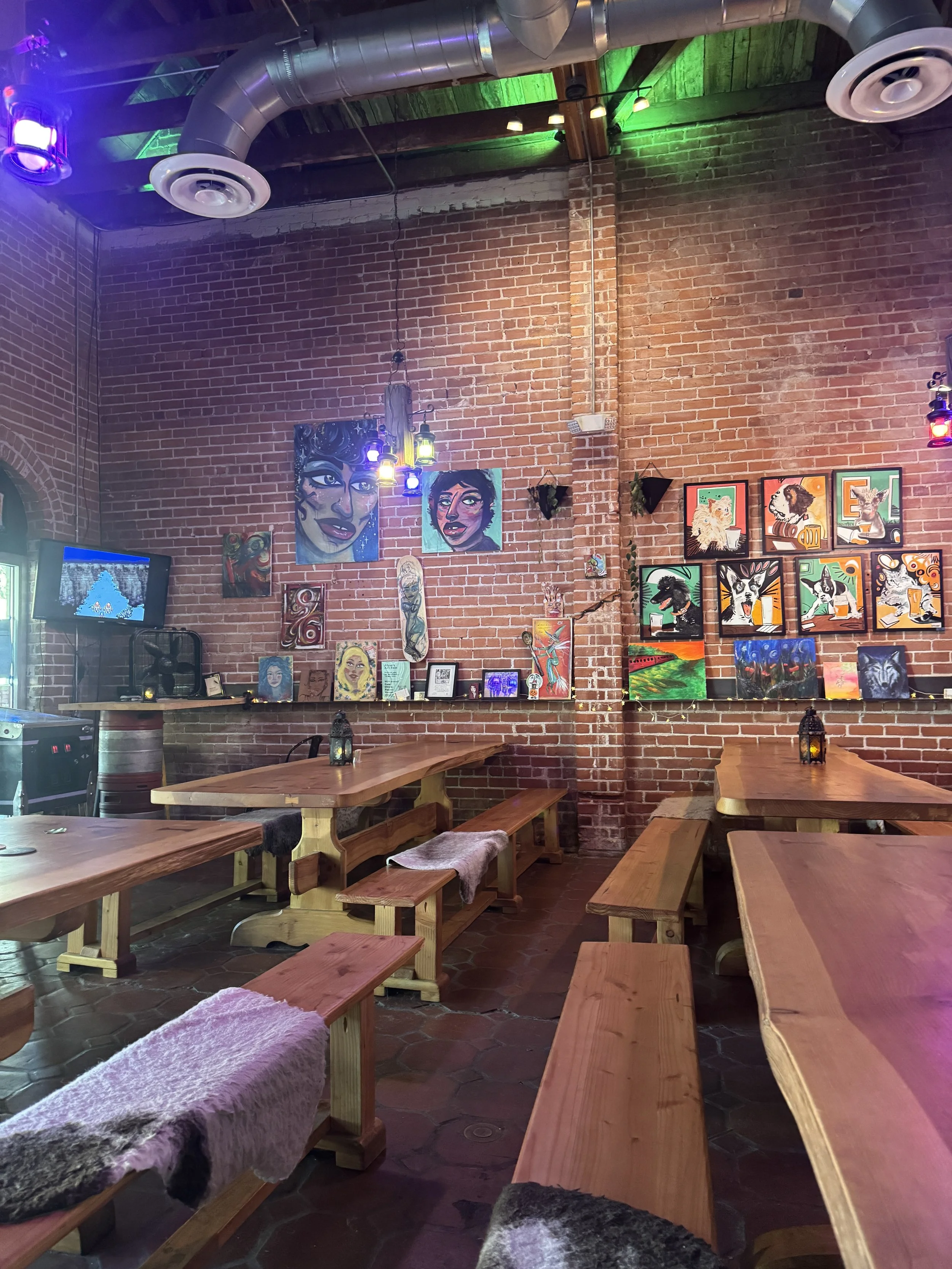 Eclectic brick-walled interior with colorful artwork, lanterns, and wooden tables at Mattie Groves Brewery in Sacramento.