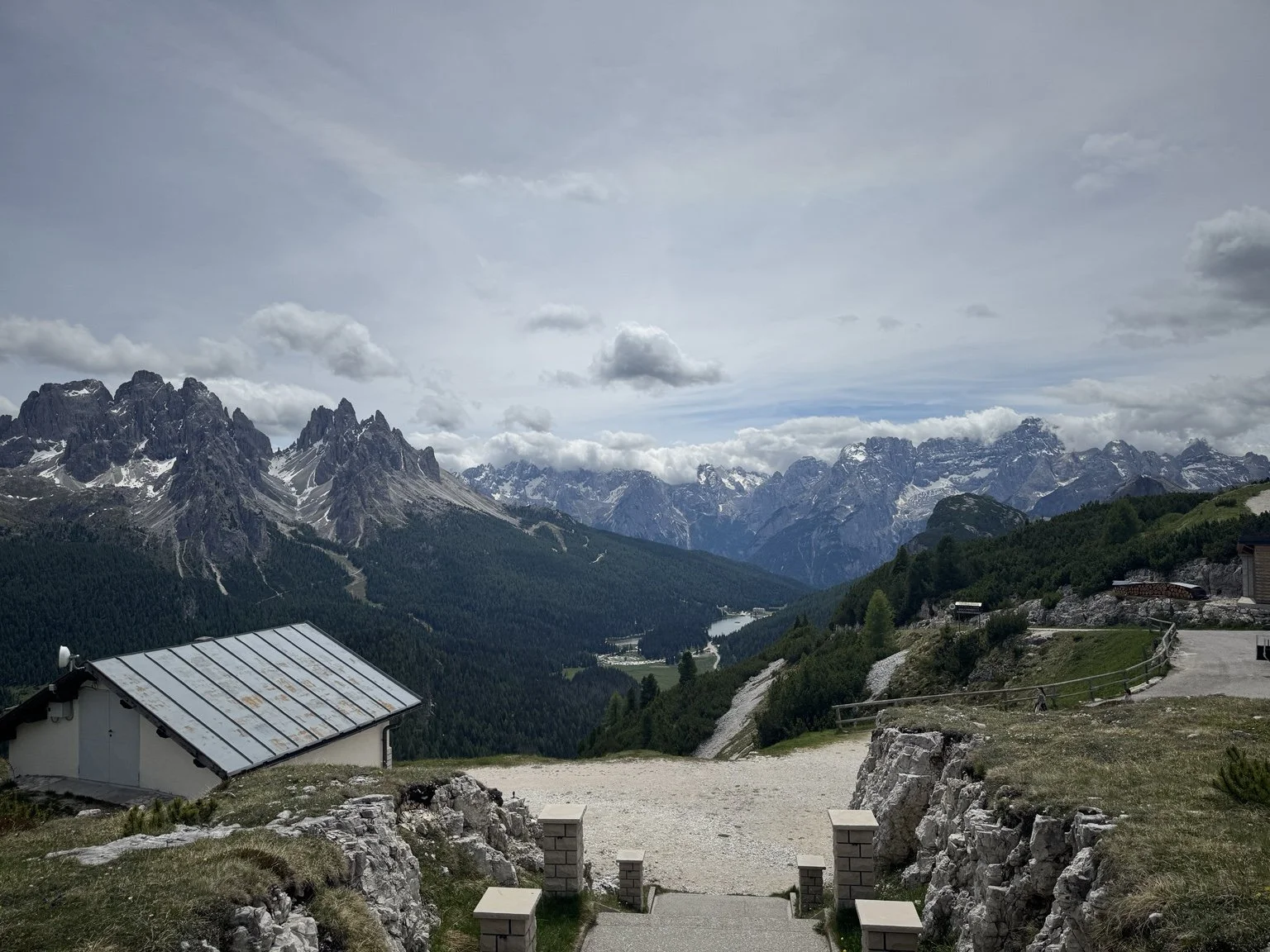 Panoramic view from Monte Piana across a forested valley to jagged Dolomite peaks.