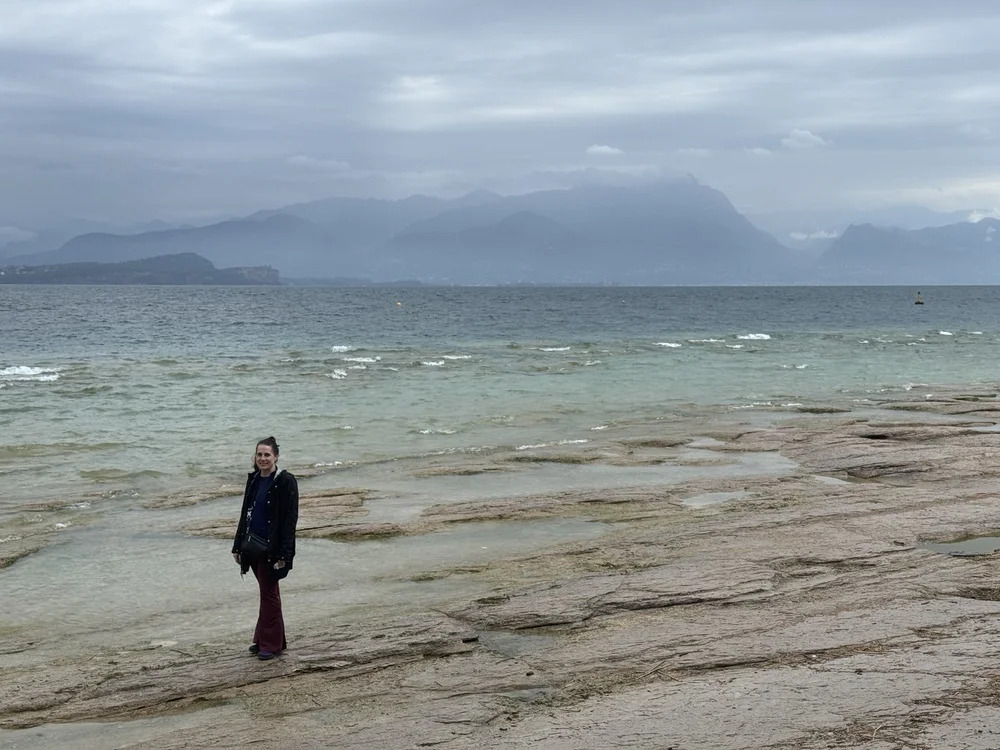 Traveler standing on the rocky shore of Lake Garda beneath misty mountains near Sirmione