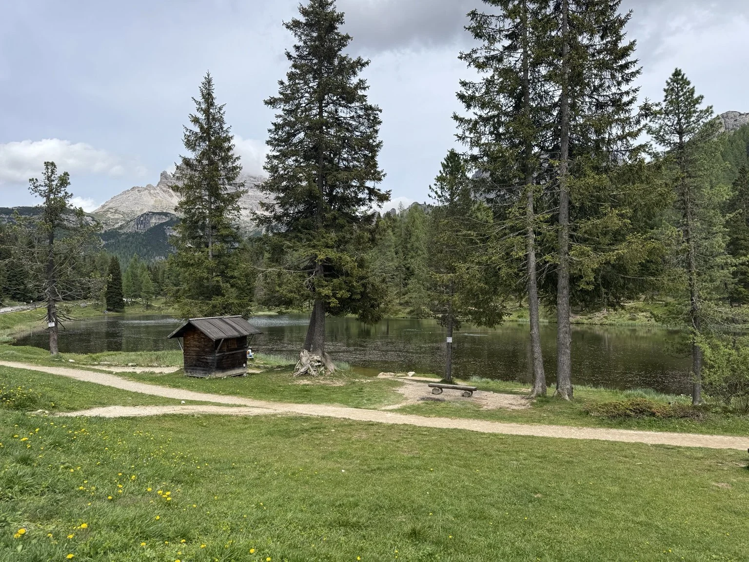 Lago d’Antorno surrounded by evergreen trees, a wooden hut and Dolomite peaks.