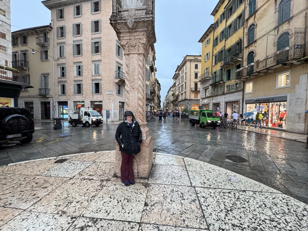 Traveler beneath a historic column on a rain-slicked street in Verona, Italy