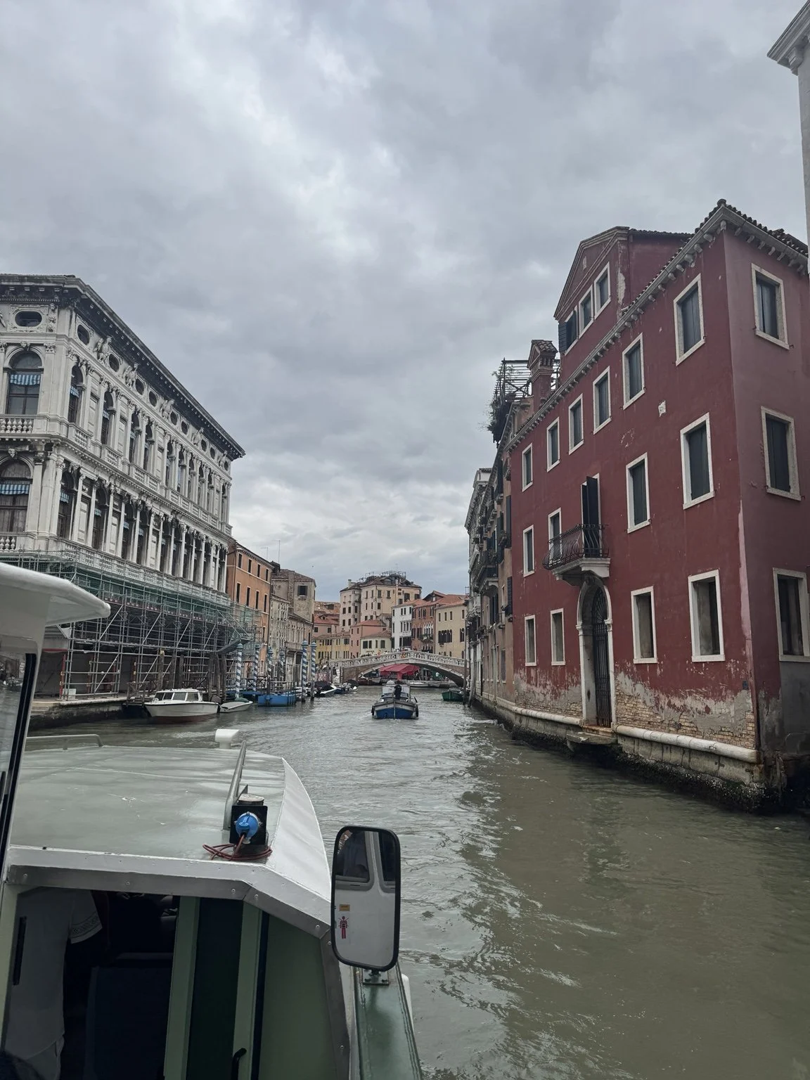 View from a Venice boat along a canal lined with historic buildings and an arched bridge.