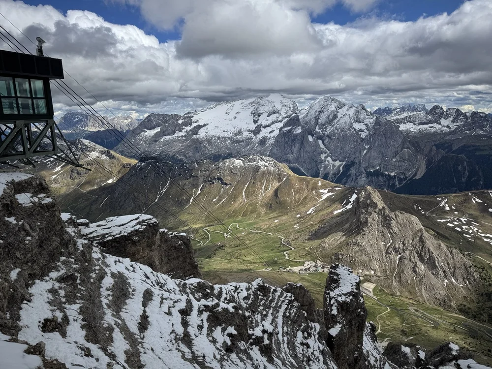 High-altitude Dolomite panorama with cable car lines, snowy peaks and winding mountain roads.