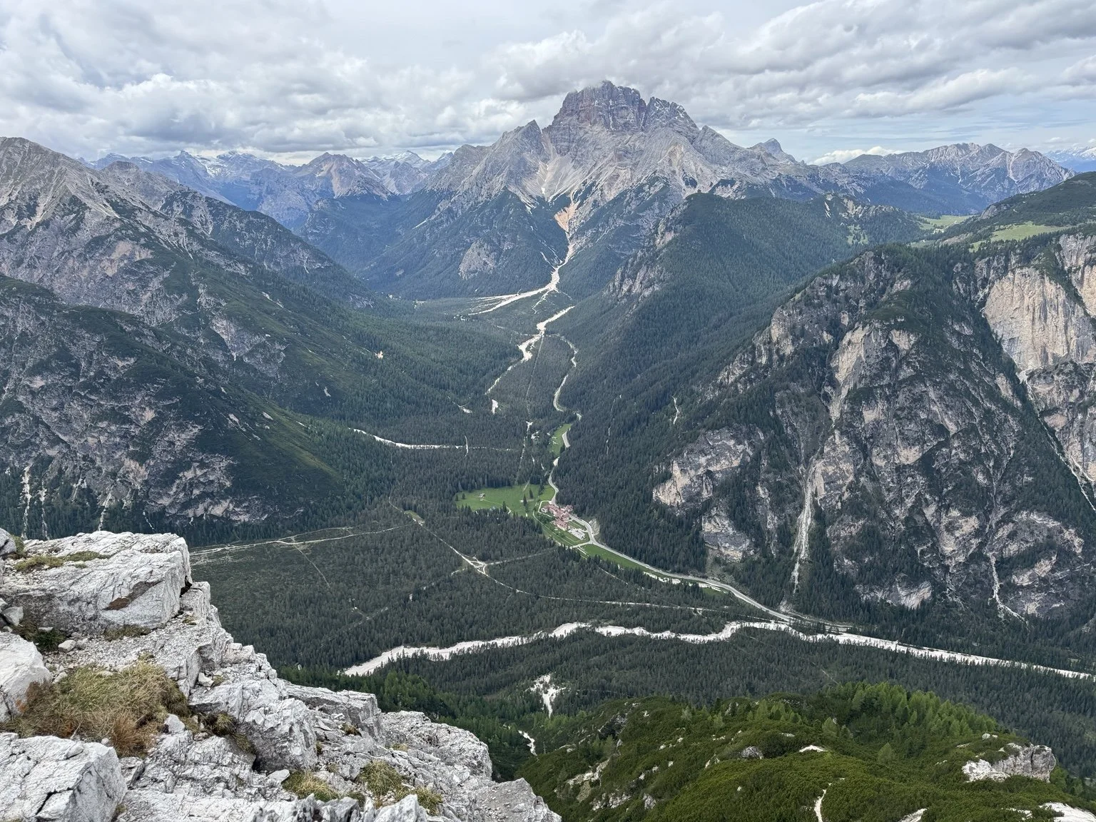 High-altitude view into a forested Dolomite valley beneath a towering mountain.