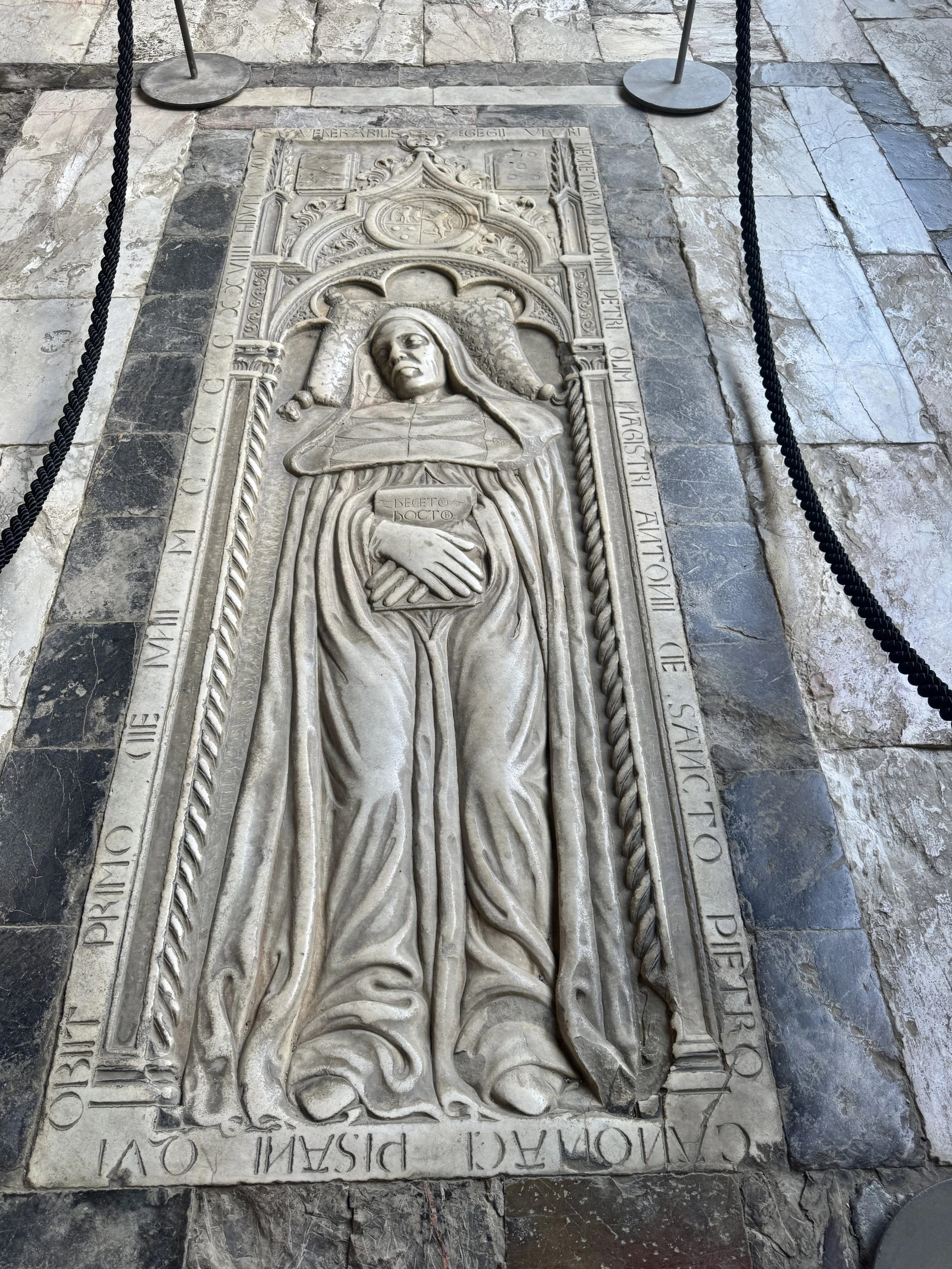 Elaborately carved floor tomb of a robed figure inside Camposanto Monumentale.