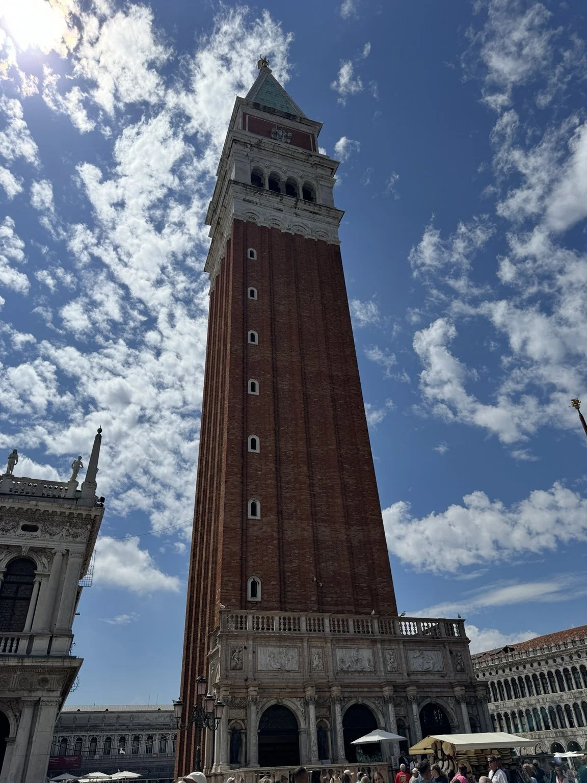 St. Mark’s Campanile rising above Piazza San Marco under scattered clouds.