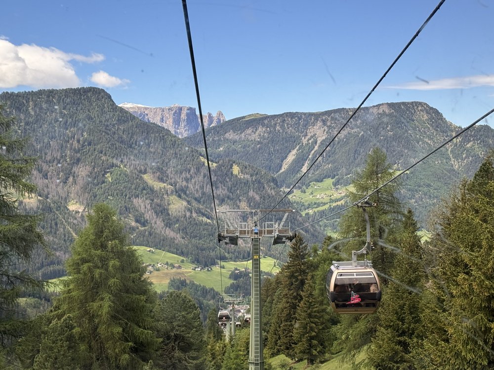 Seceda cable car descending above Val Gardena with forested mountains beyond.