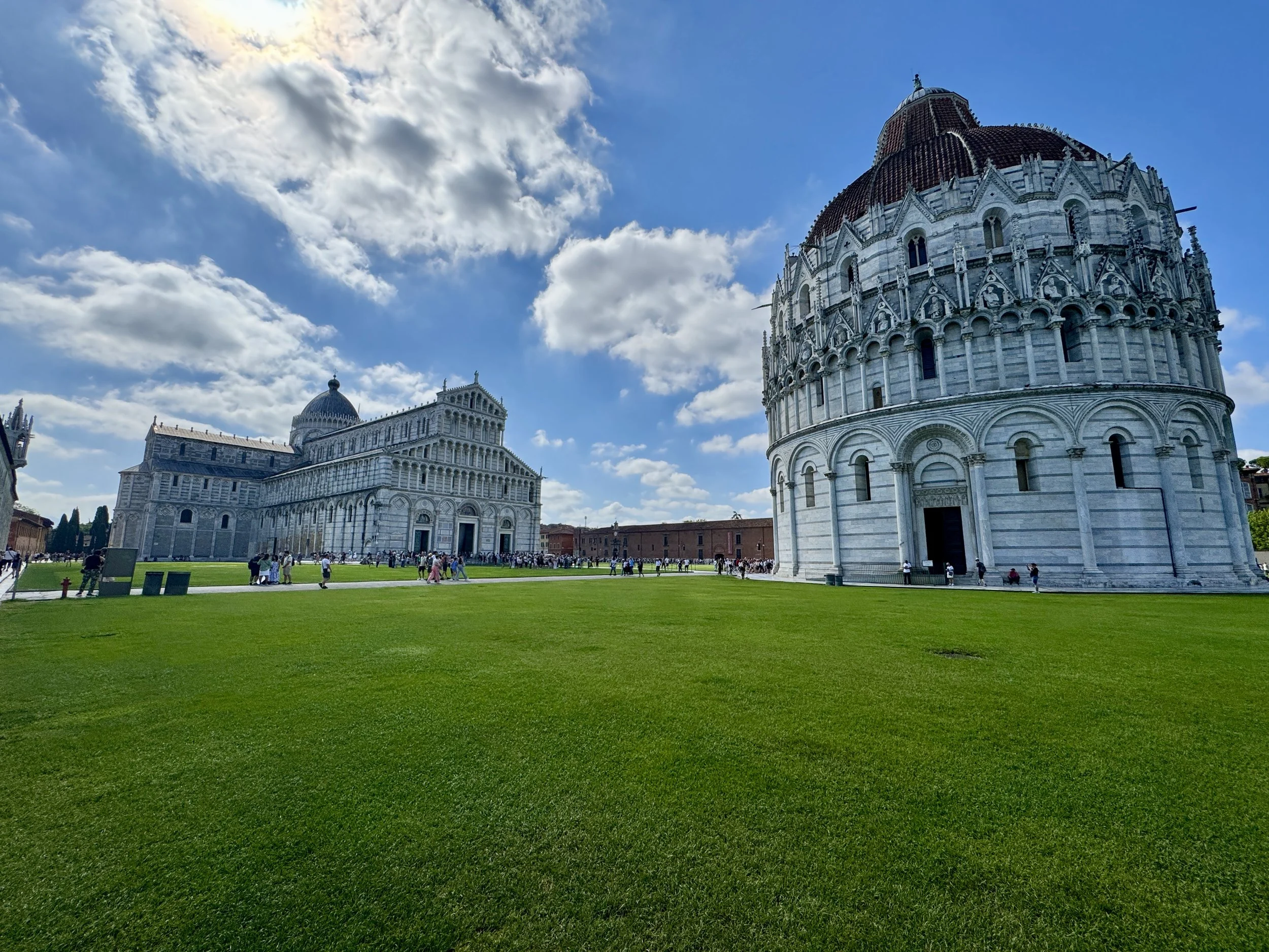 Wide view of Pisa Cathedral and Baptistery across the green lawn of Piazza dei Miracoli.