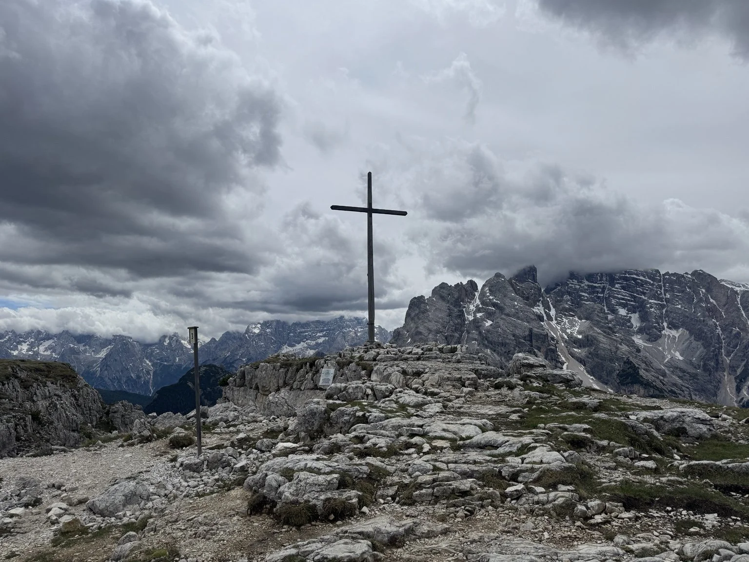 Large wooden memorial cross on Monte Piana beneath storm clouds and rugged peaks.