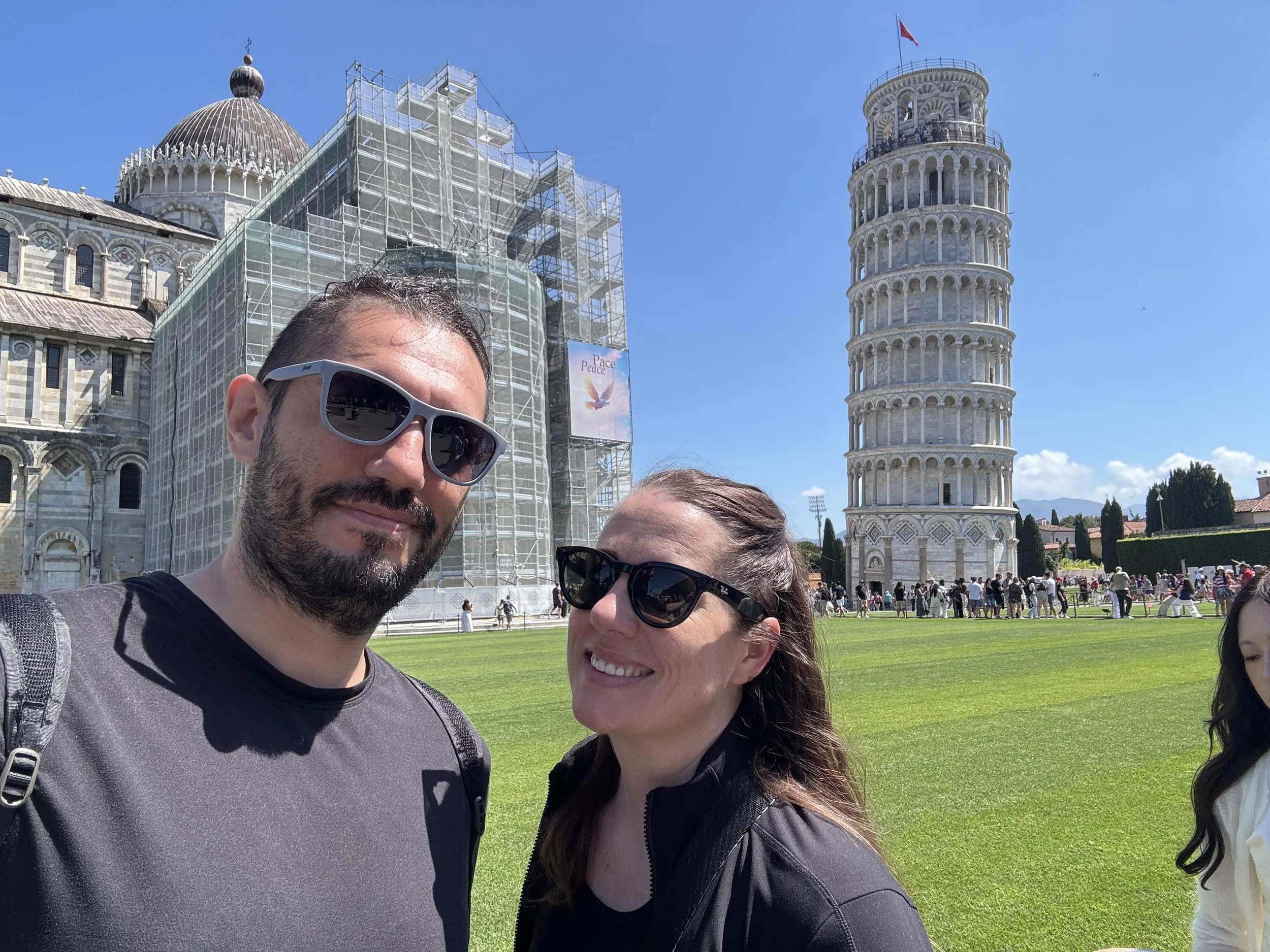 Couple taking a travel selfie with Pisa Cathedral and the Leaning Tower behind them.