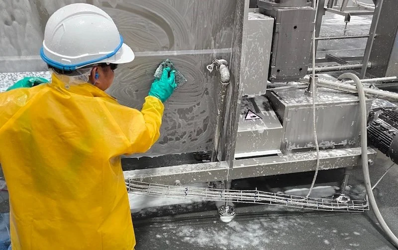 People First Sanitation crew member in rain gear scrubbing plant equipment