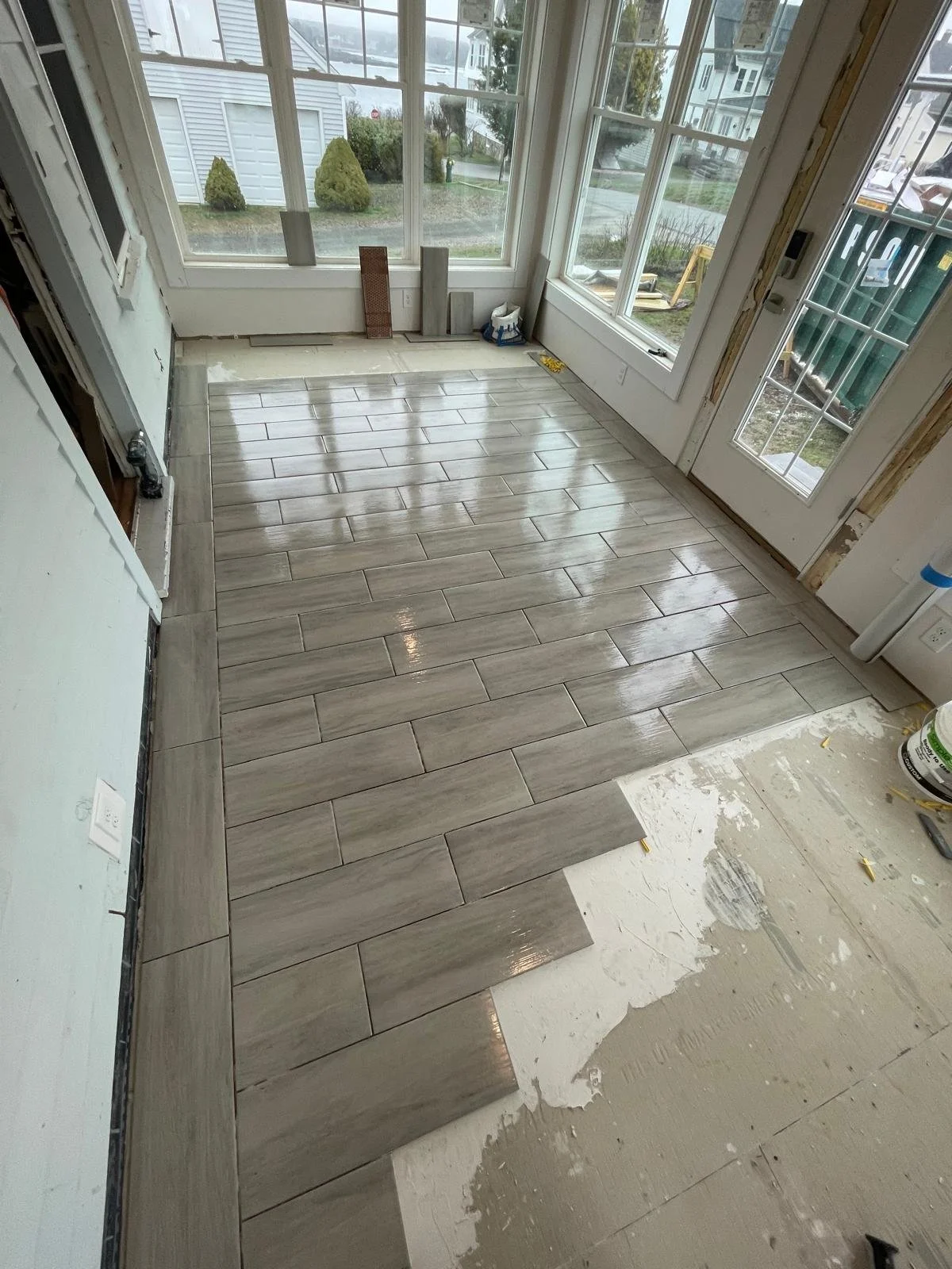 Gray wood-look plank tile floor laid out in the three-season porch with water view beyond, York ME