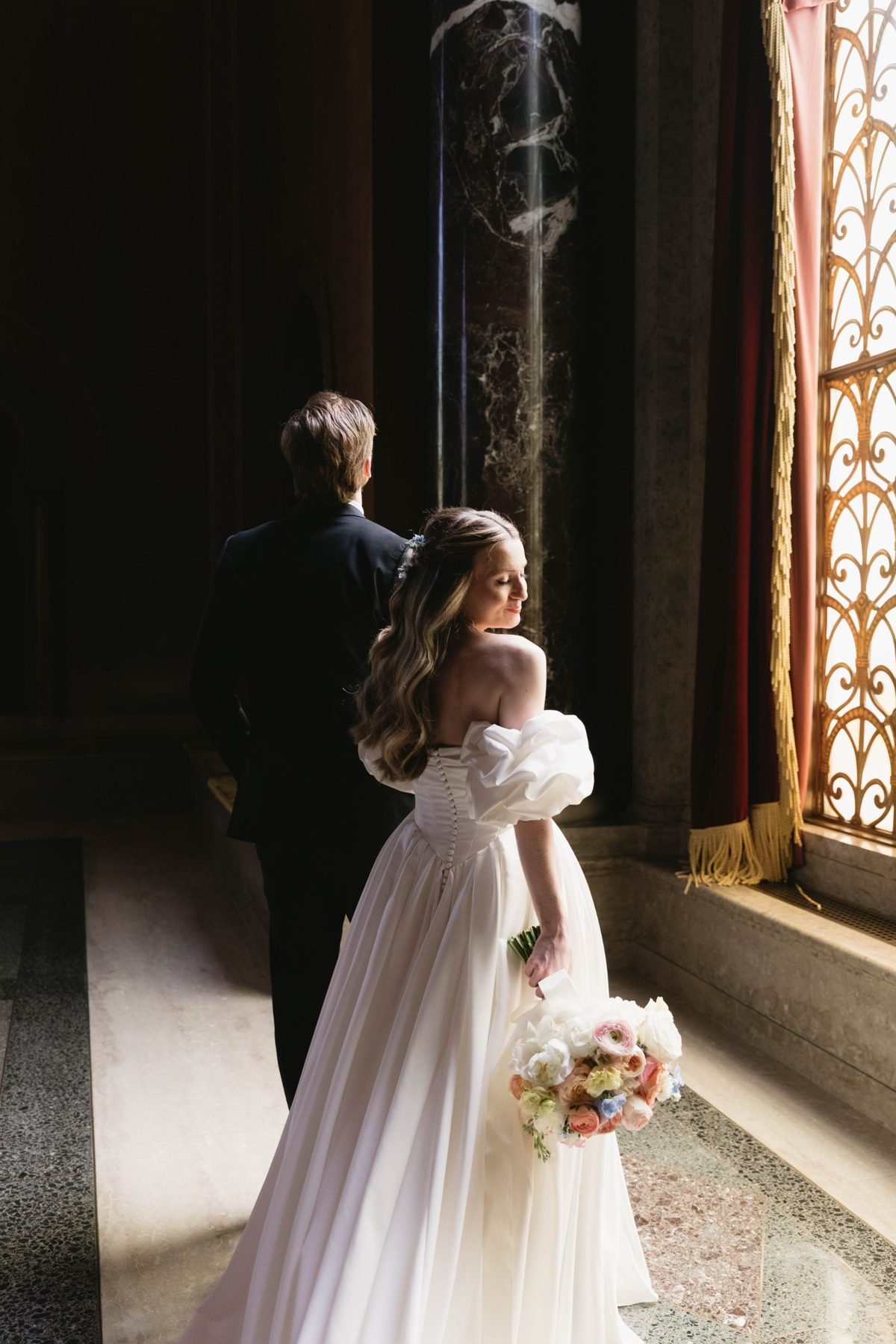 Bride carrying her bouquet through a marble hall beside a gilded window