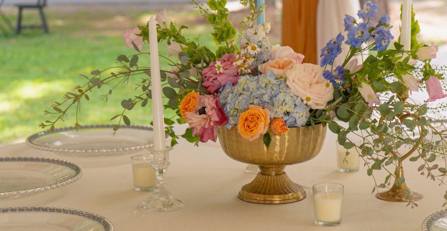Brass compote centerpiece with trailing eucalyptus and taper candles on a round table