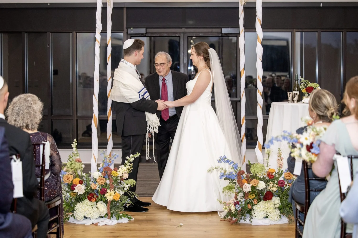 Couple beneath a draped chuppah framed by two floral meadows of delphinium, garden roses, amaranthus, dahlias and hydrangea