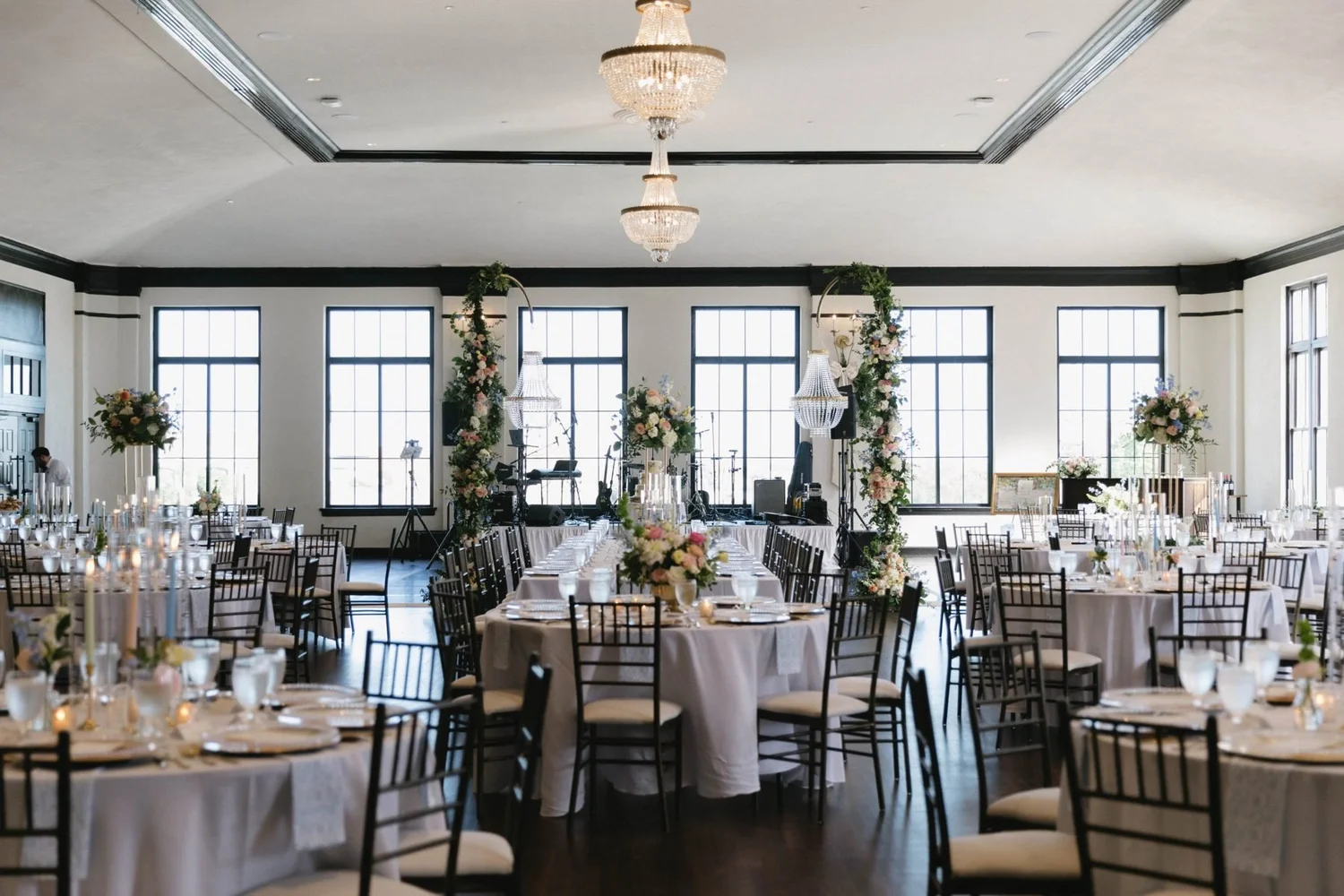 The Hotel 1928 ballroom set for reception, with flower-wrapped hoop installations framing the stage beneath crystal chandeliers
