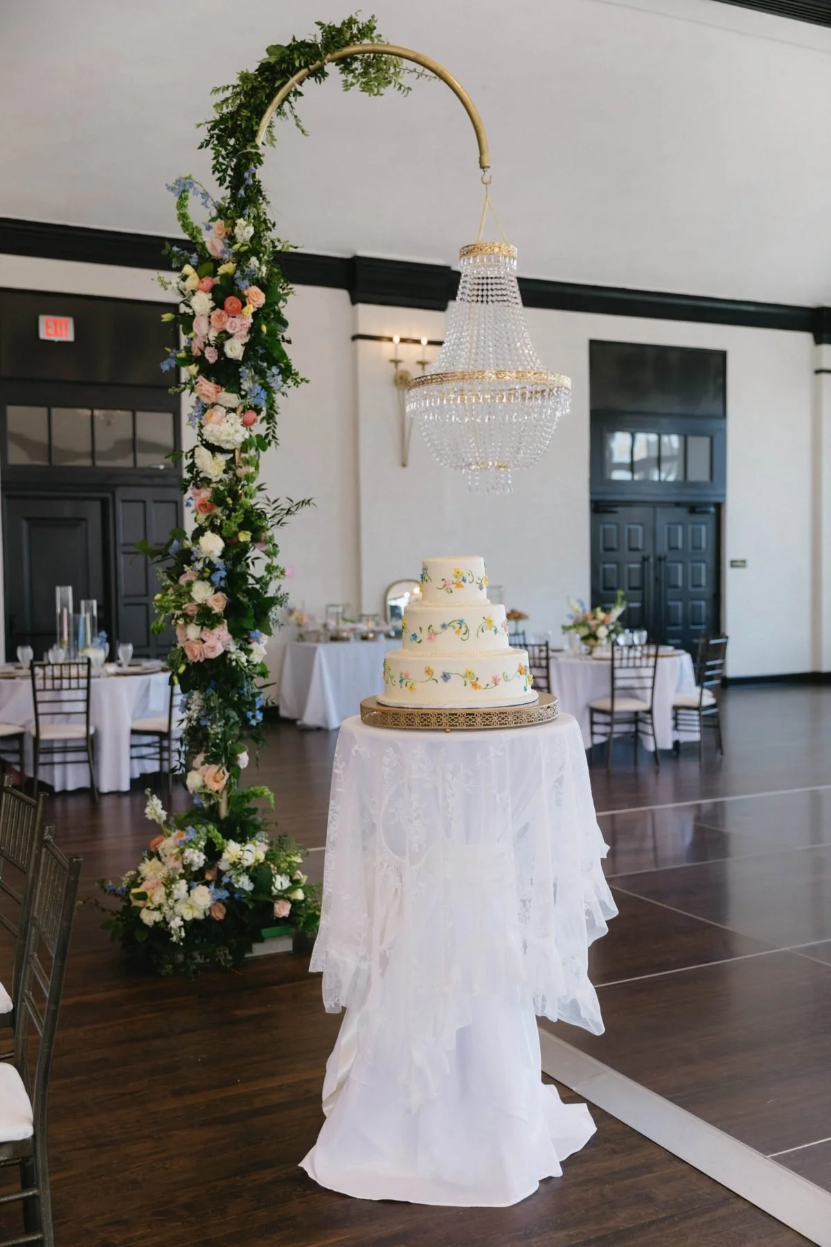 Hoop installation with a crystal chandelier above a three-tier cake on a lace-draped table