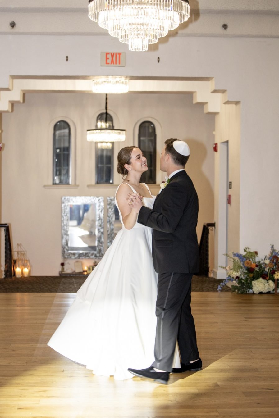 First dance beneath crystal chandeliers beside a floor arrangement