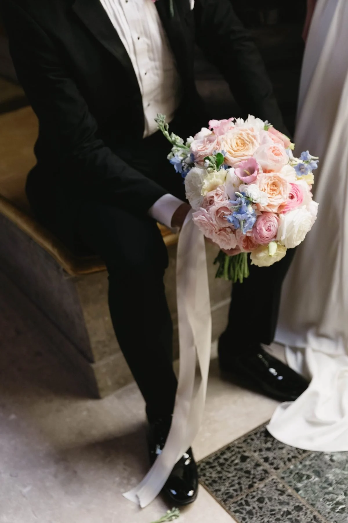 Bridal bouquet with long ivory silk ribbons resting against a black tuxedo