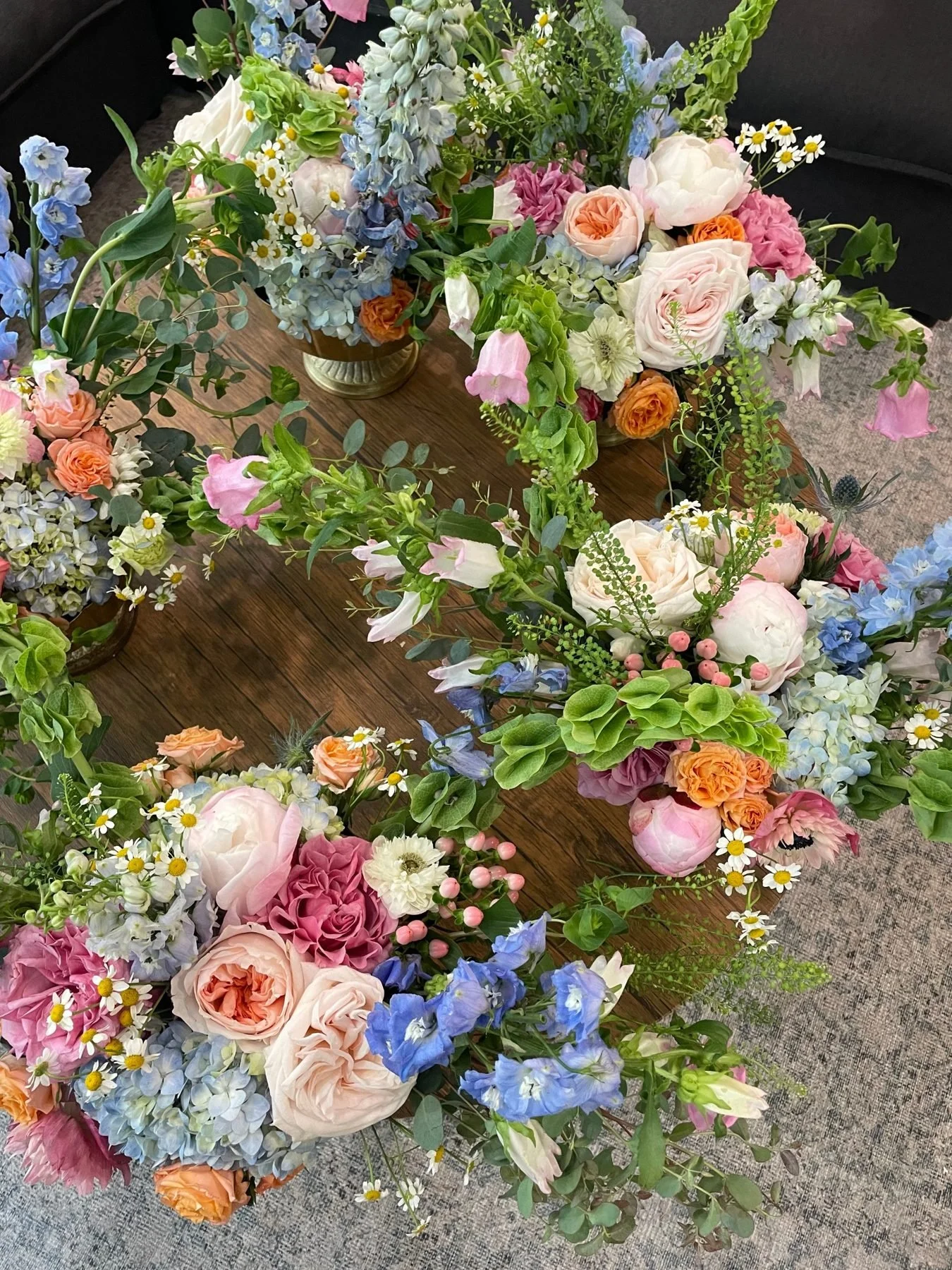 Overhead view of brass compotes filled with peonies, garden roses, delphinium, hydrangea and bells of Ireland