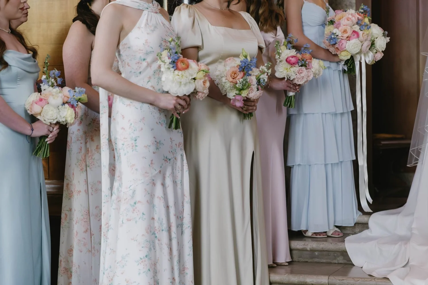 Bridesmaids in pastel and floral gowns holding garden bouquets