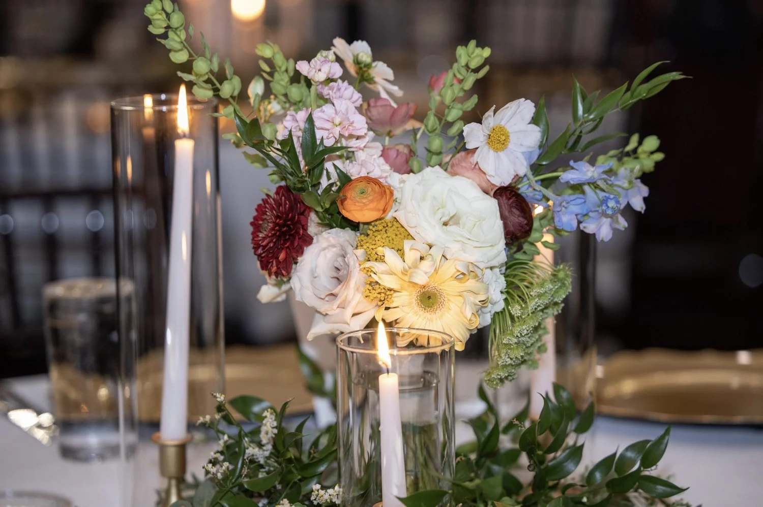 Jewel-toned centerpiece of dahlia, ranunculus, garden rose and delphinium by candlelight
