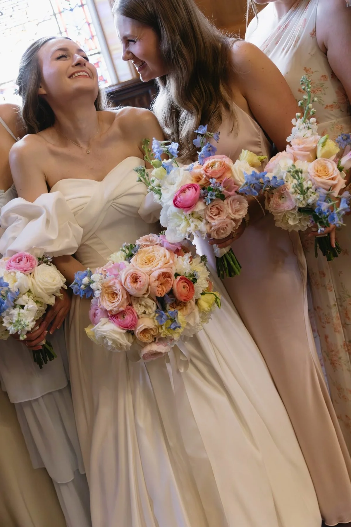 Bride and bridesmaid laughing with bouquets of garden roses and ranunculus