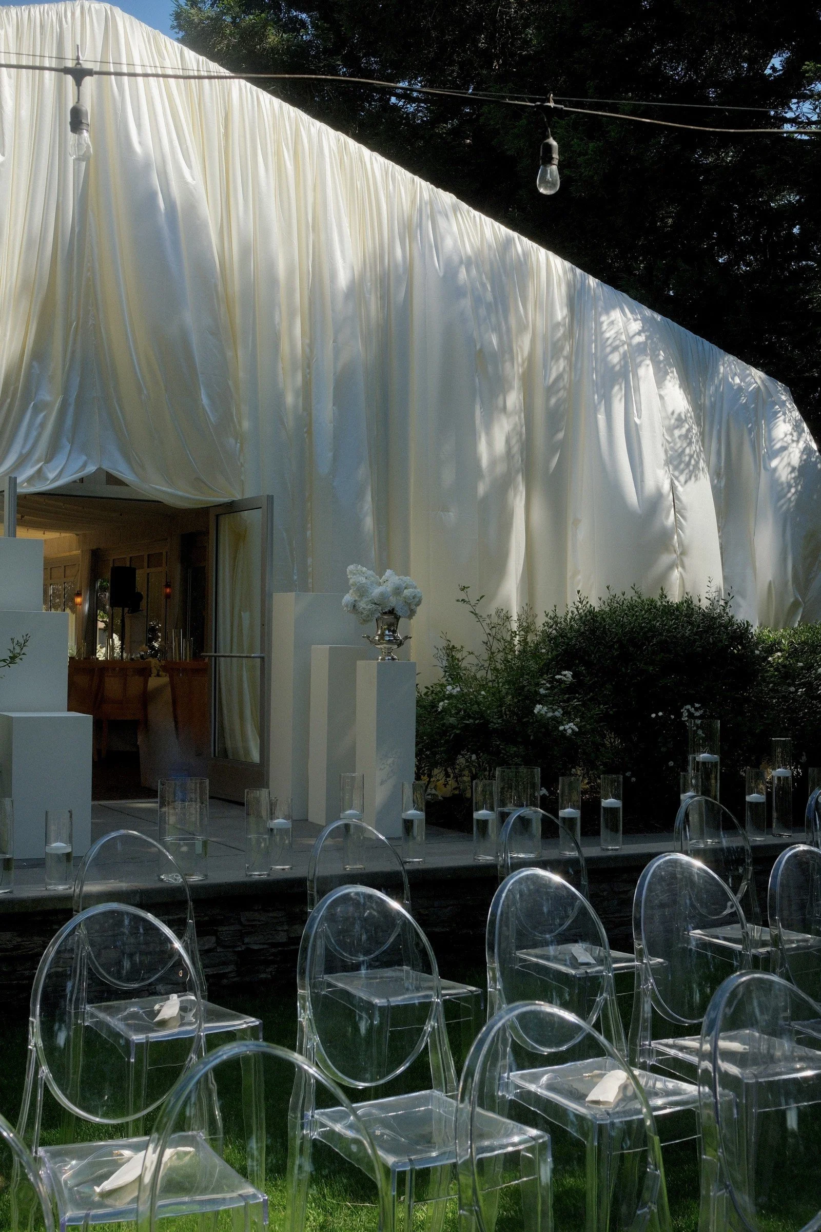 White draping behind transparent ceremony chairs