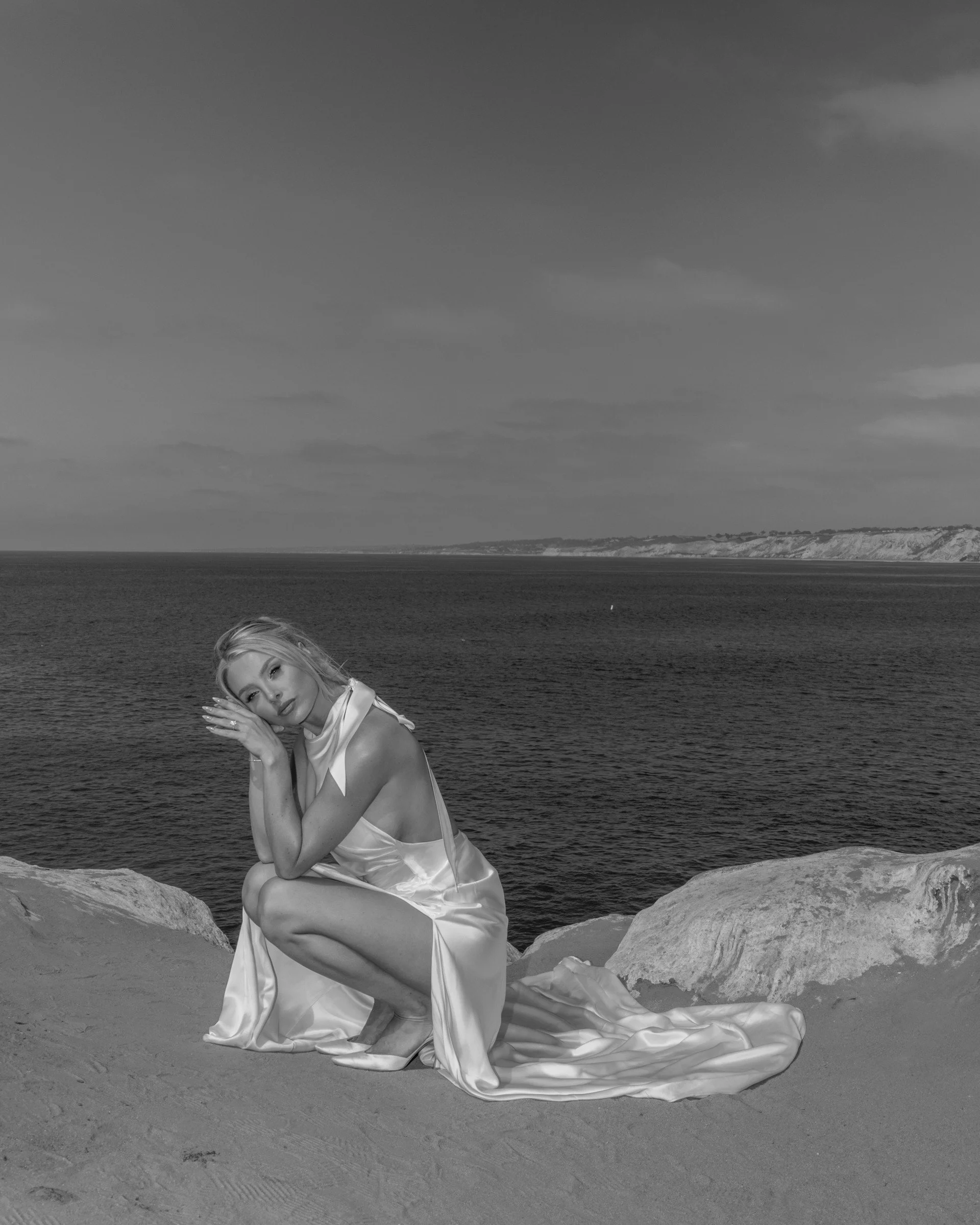 Black-and-white portrait of a bride and her train beside the sea