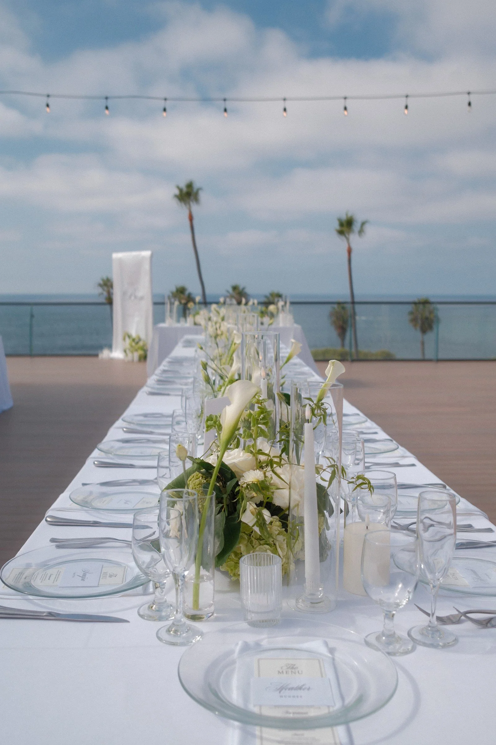 White floral arrangements along an oceanfront reception table