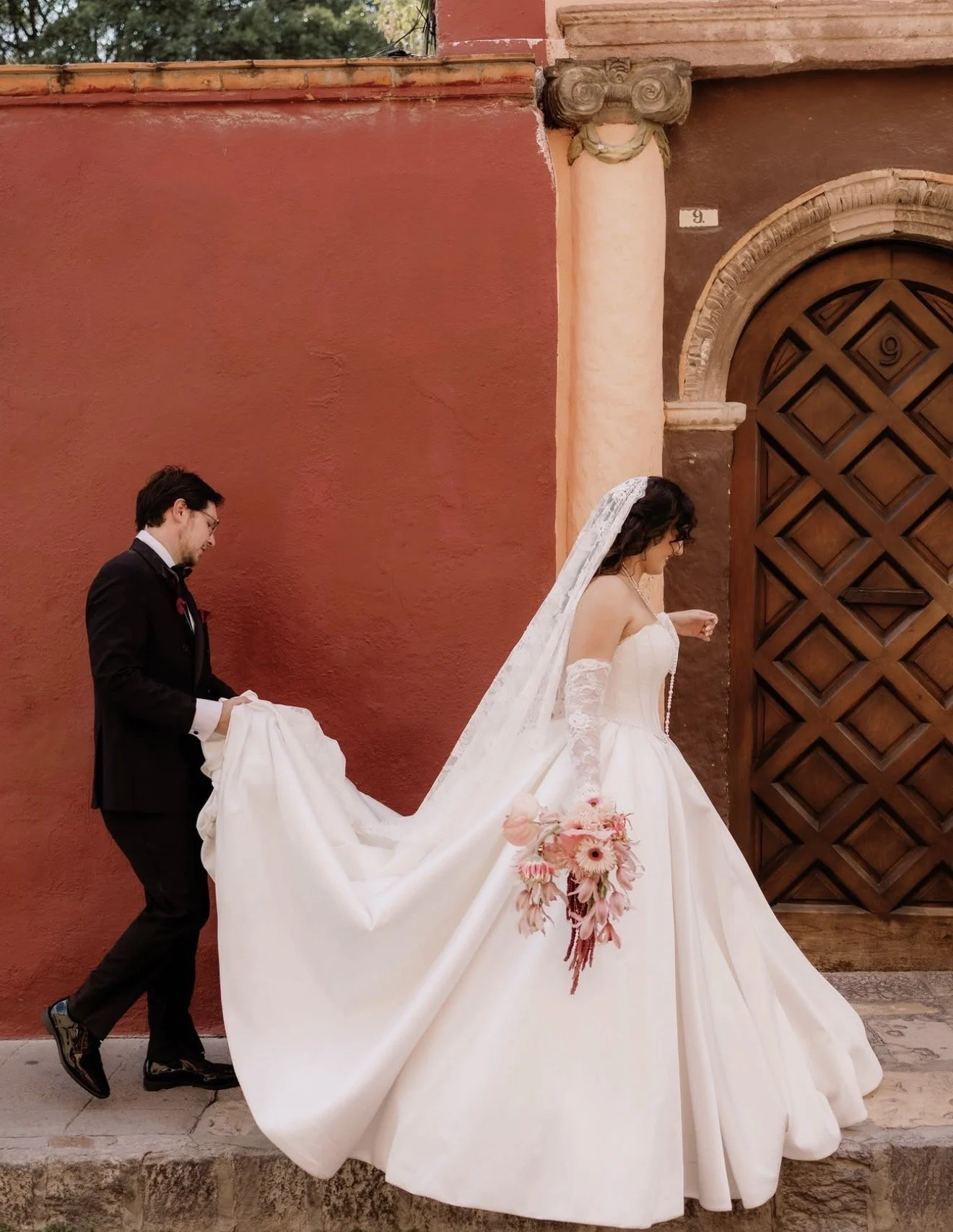 Newlyweds beside a terracotta wall with a cascading pink bouquet