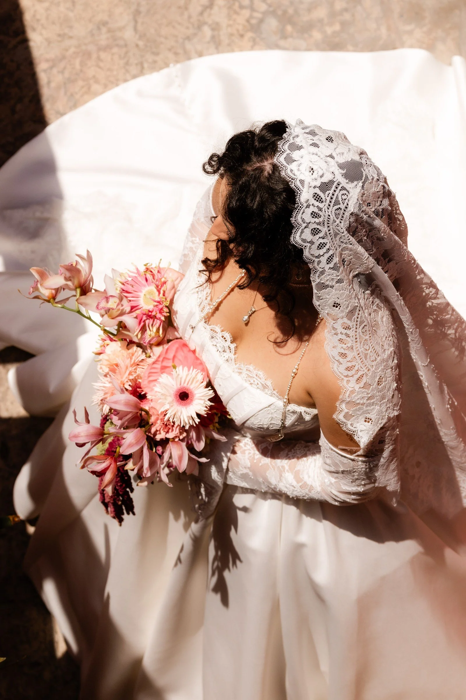 Bride carrying pink flowers beneath a lace veil