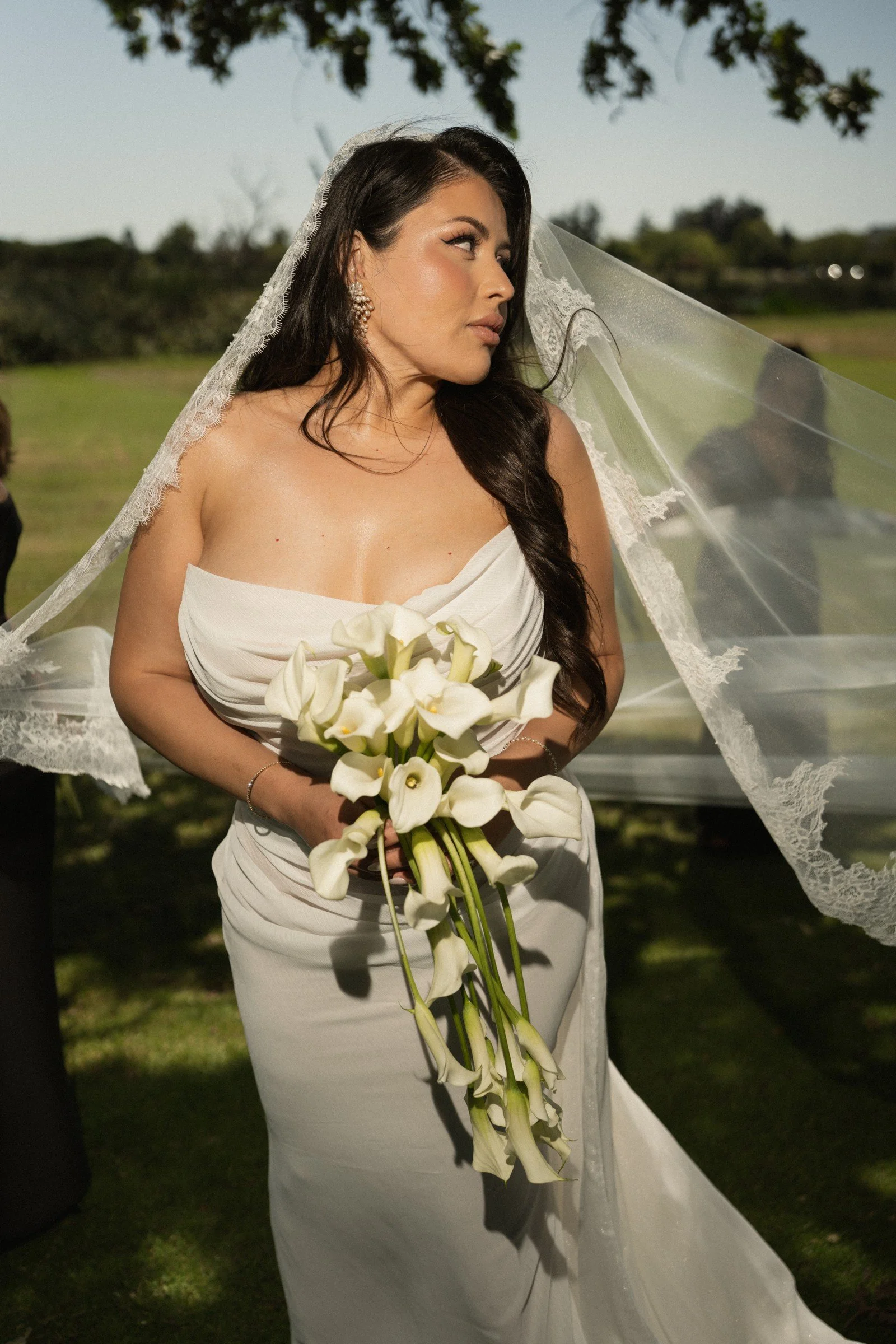 Bride holding a white bouquet beneath the trees