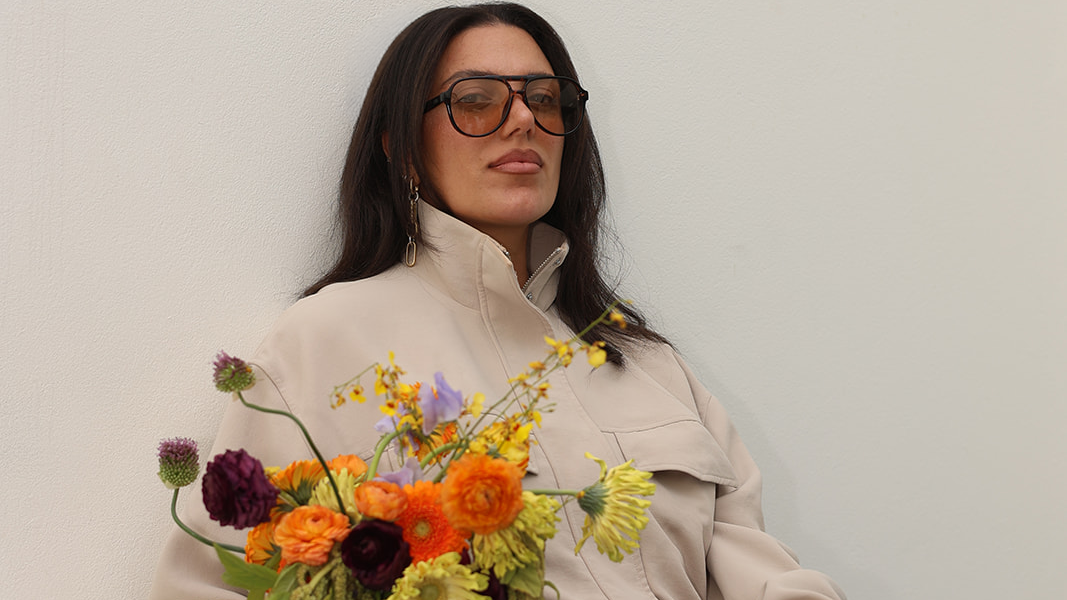 Arpy holding a colorful bouquet, wearing sunglasses and a cream jacket