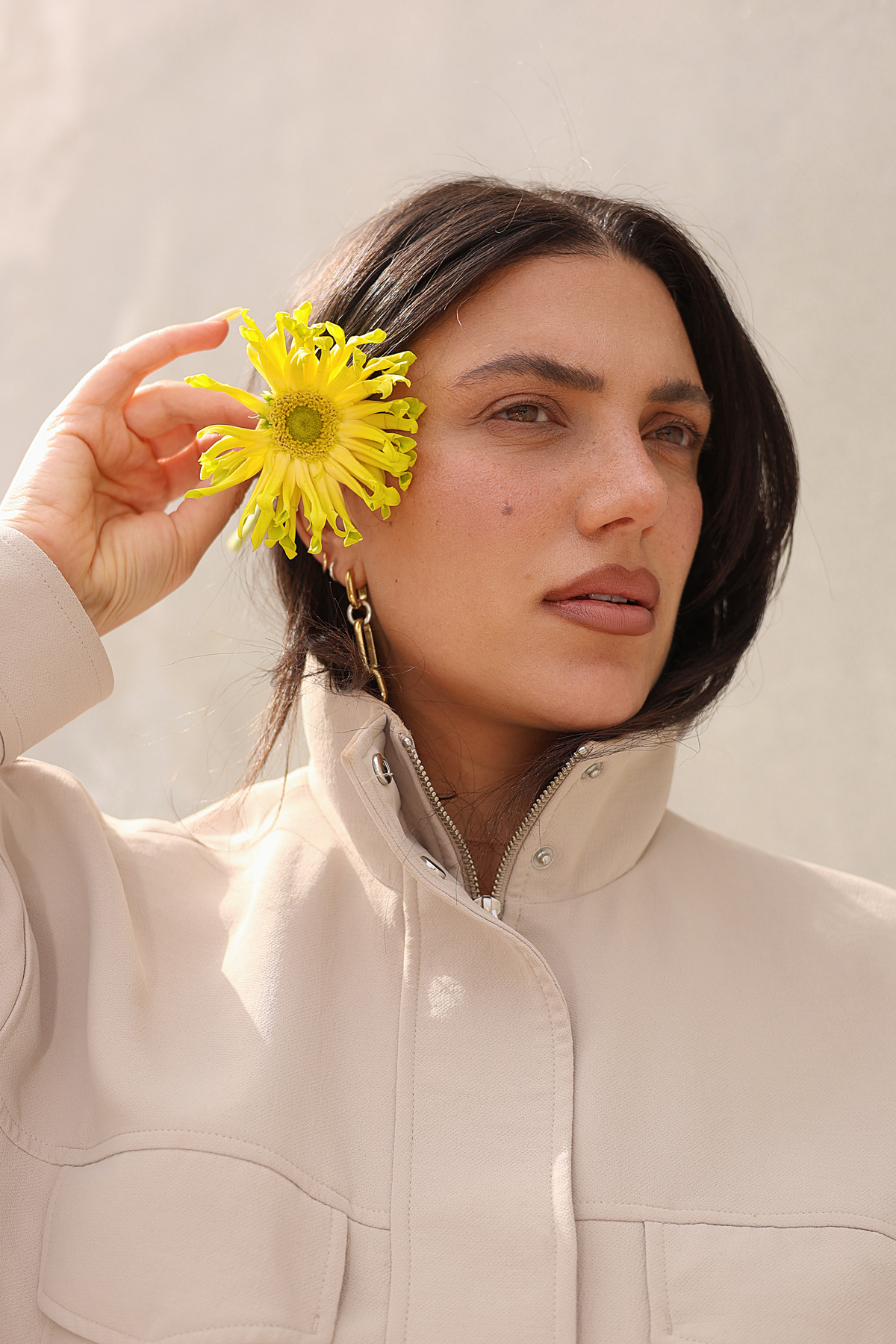 Arpy holding a yellow flower beside her face in warm sunlight