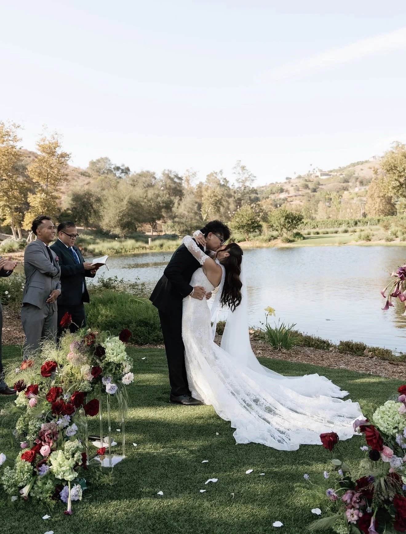 Newlyweds kissing beside a lake surrounded by colorful floral arrangements