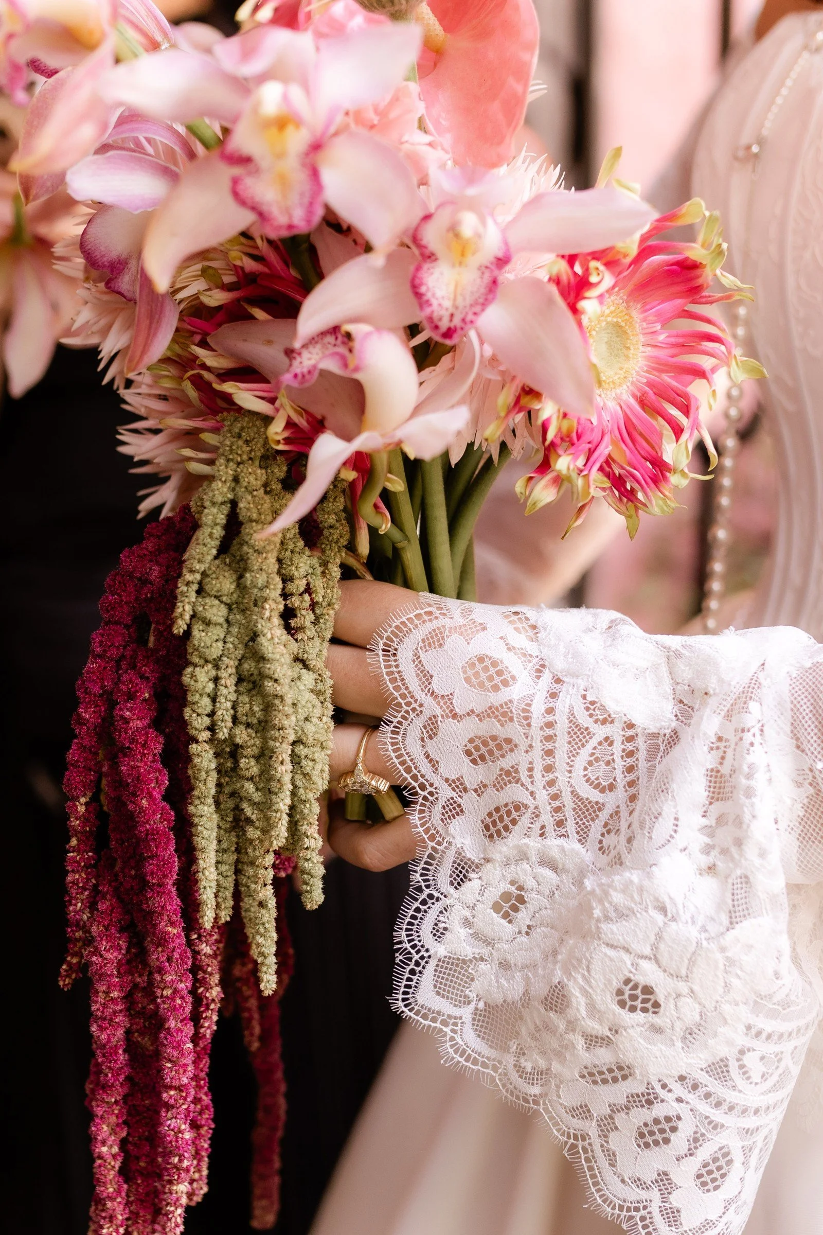 Close-up of a pink bridal bouquet and lace sleeve