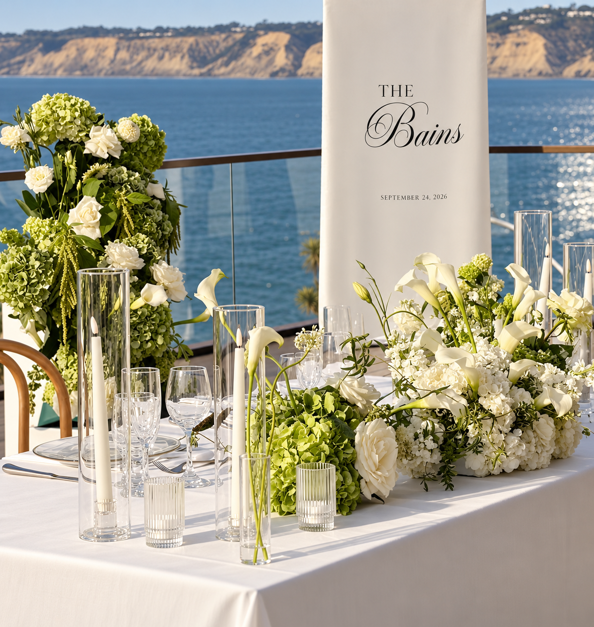 Personalized wedding signage beside white and green florals overlooking the ocean