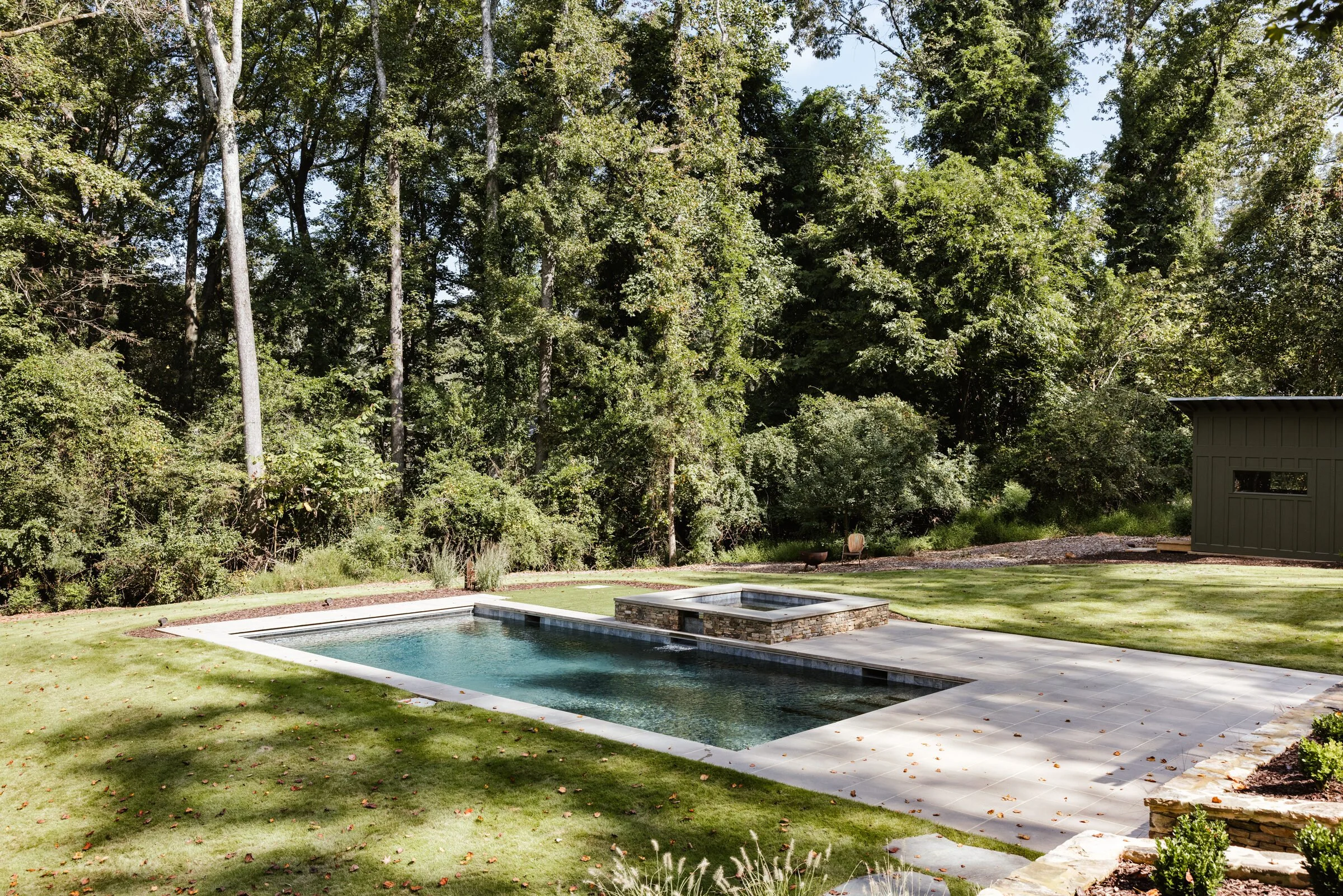 Dark-plaster pool framed by lawn and mature hardwoods
