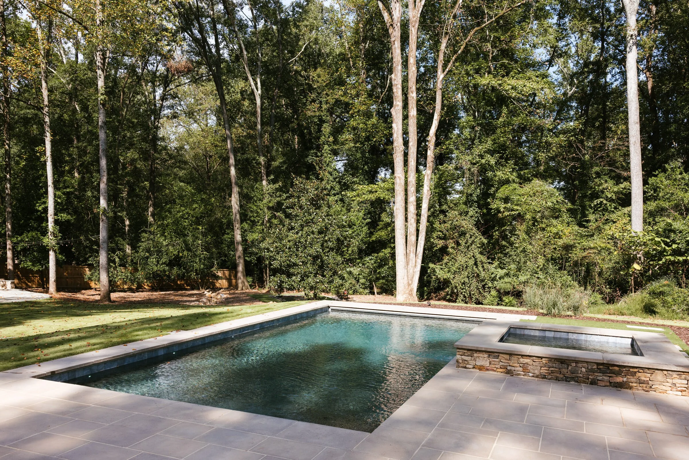 Stone-walled pool and raised spa set below a wooded Athens home