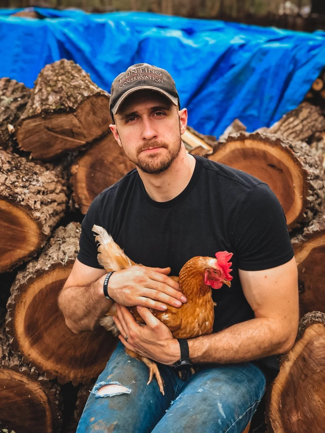 Cody Lutz holding a chicken beside a stack of firewood