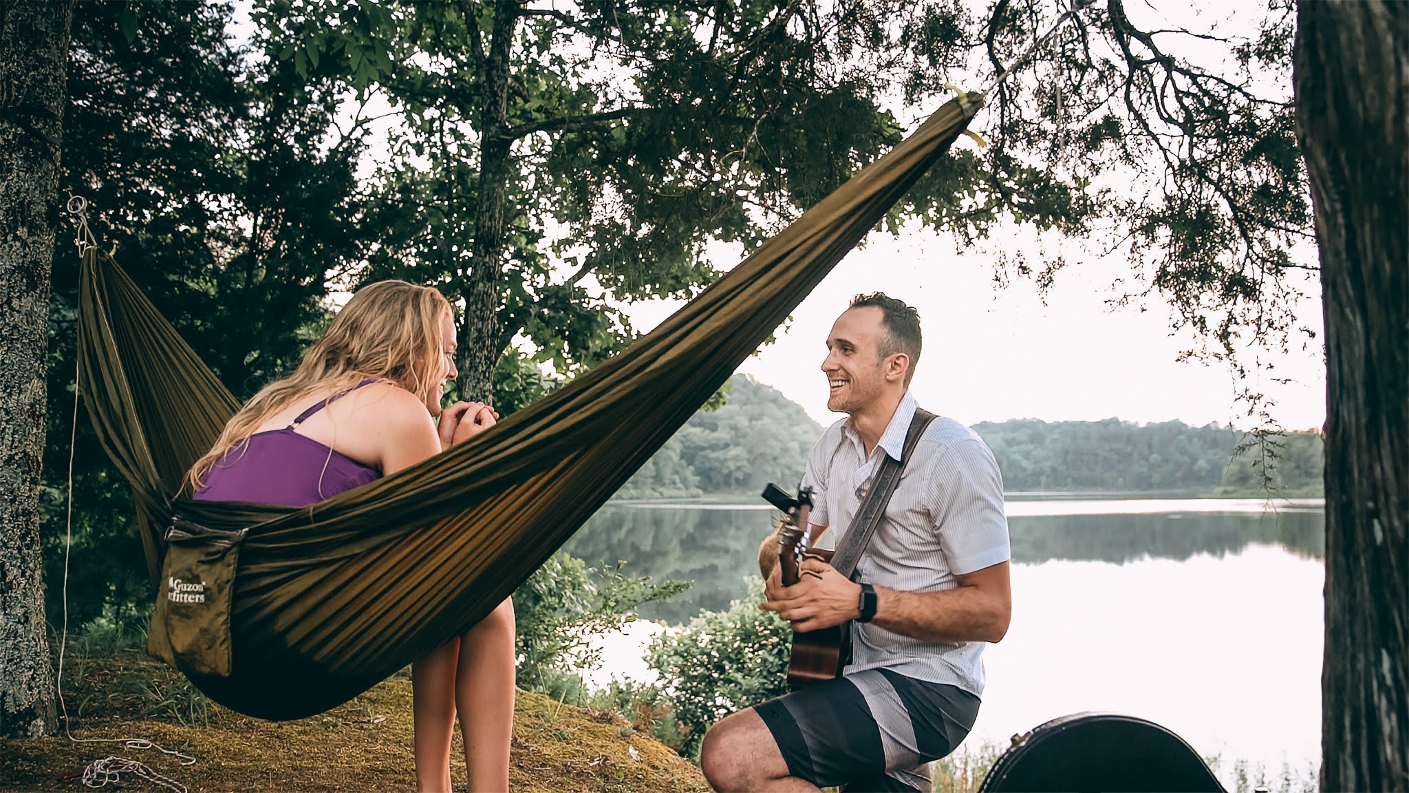 Cody playing guitar for Lucy beside a lake