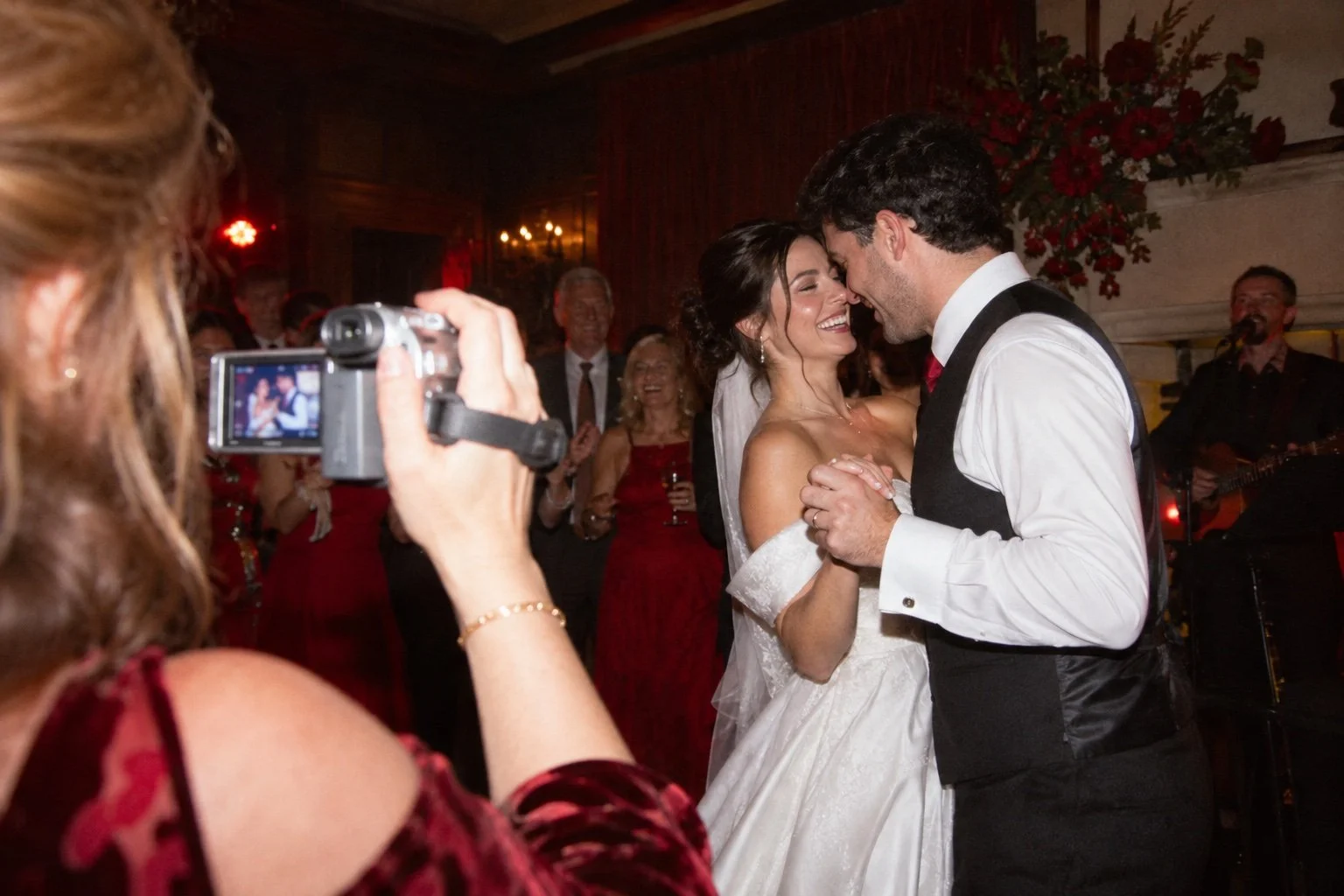 Illustrative wedding scene: a guest films a couple dancing on a retro camcorder