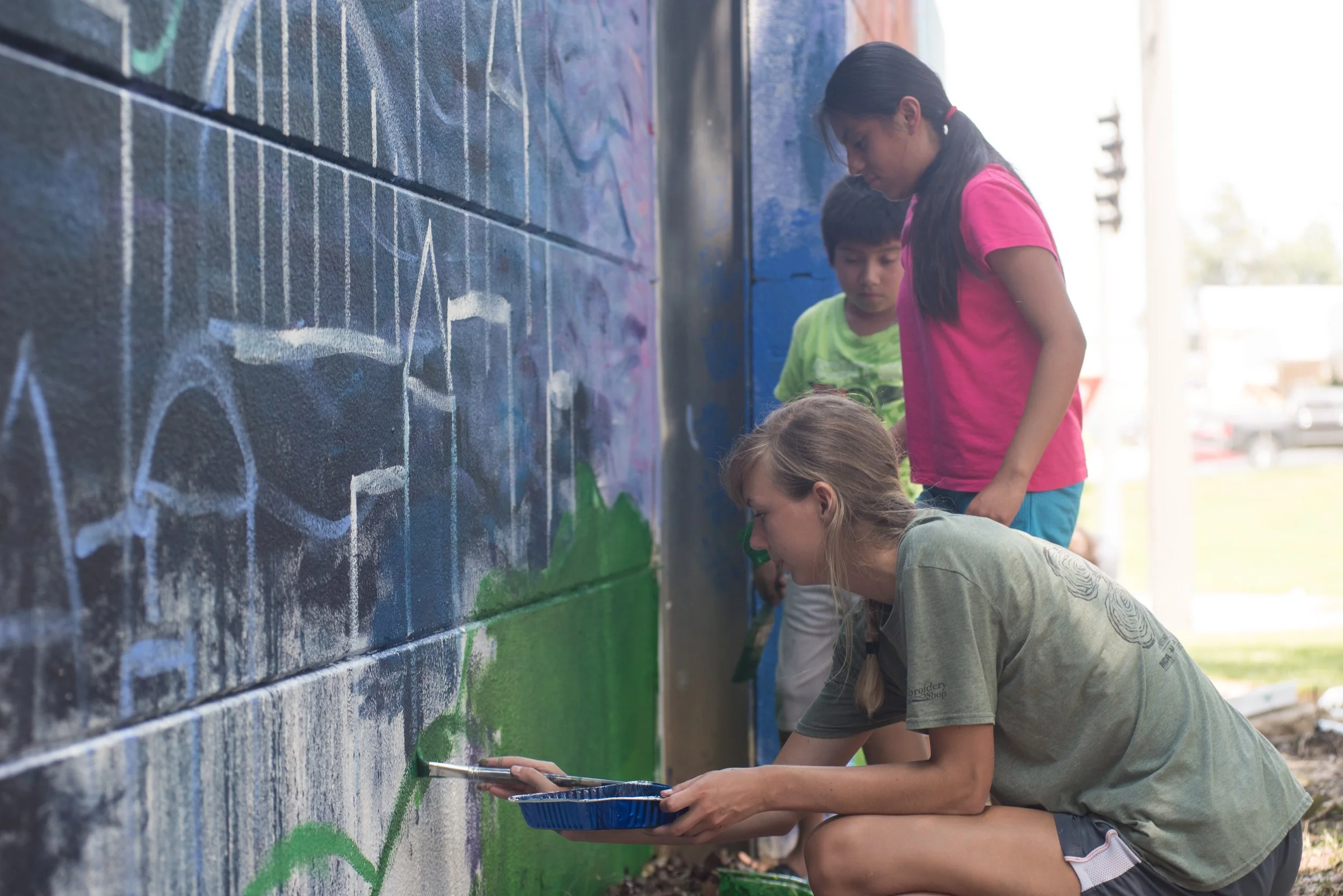 A woman and two children paint a mural on a wall.