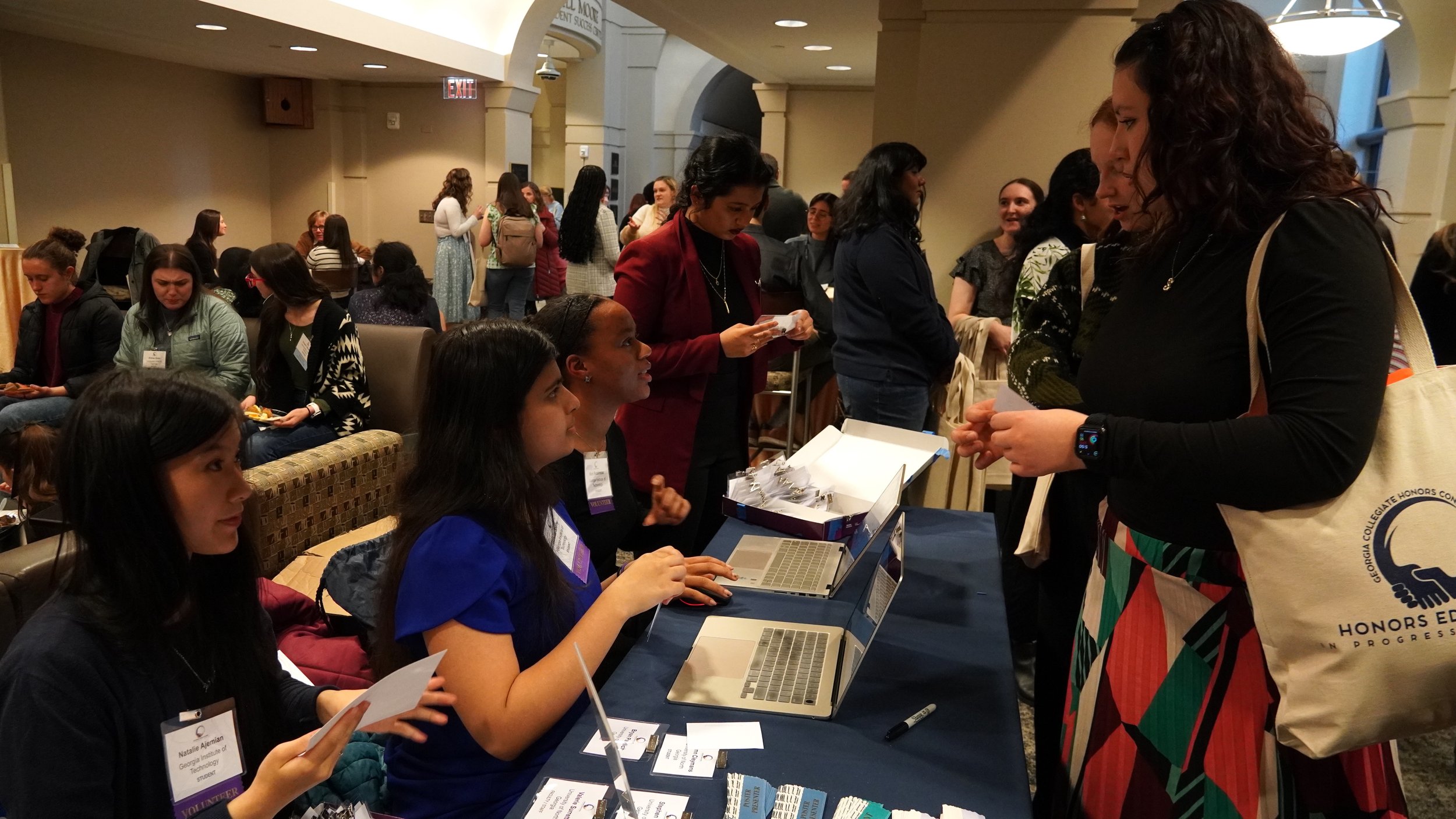 A group of women sit at a table and greet guests to a conference.
