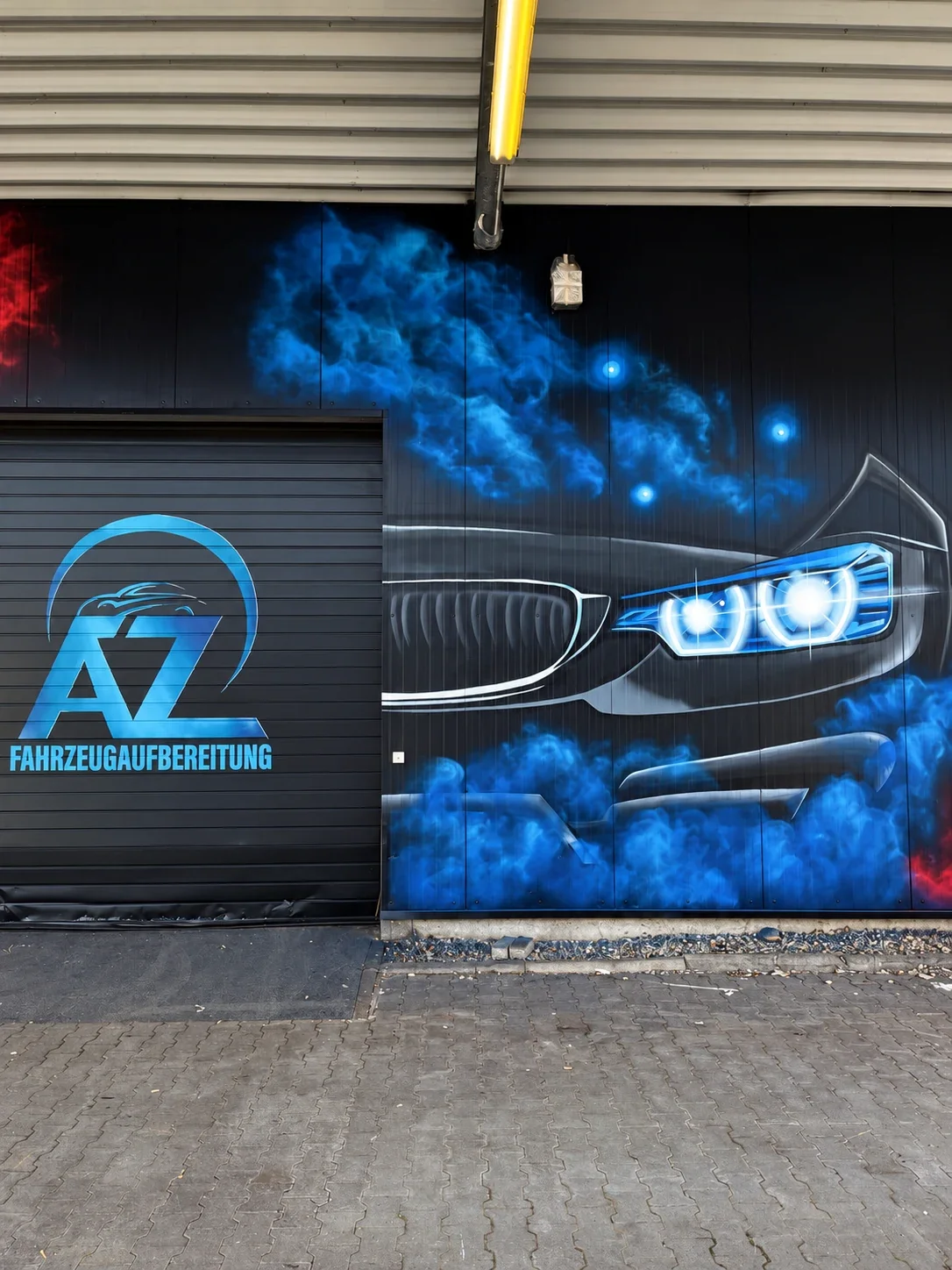 Blaue Fahrzeugfront mit leuchtenden Scheinwerfern und Werkstattlogo auf der Blechfassade in Erlensee