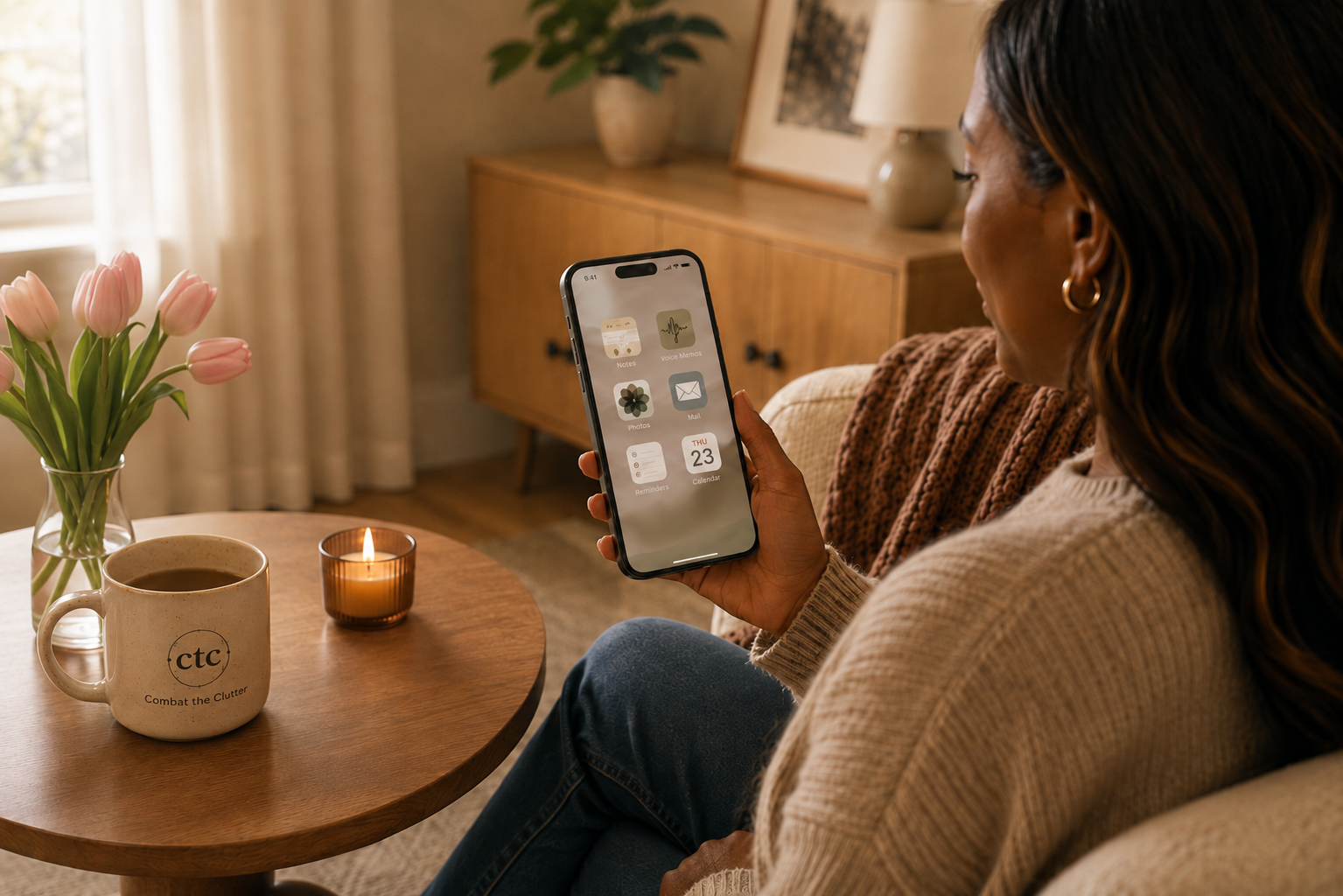 Woman using a smartphone with everyday digital tools visible on screen beside tulips and a Combat the Clutter mug.